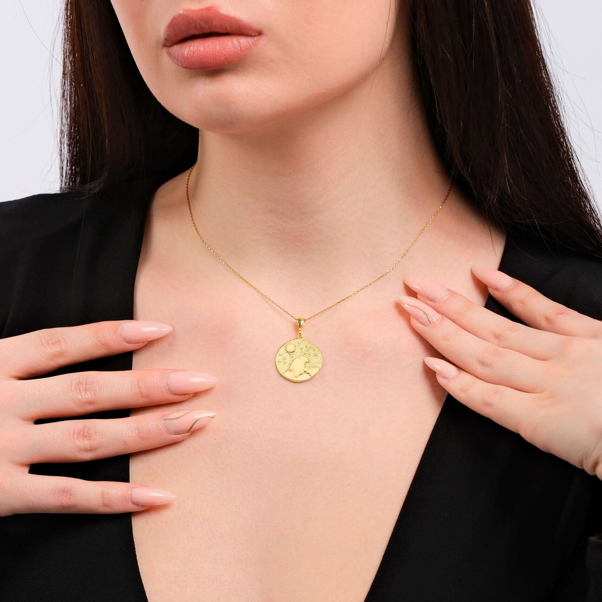 Woman wearing elegant gold necklace with round pendant, showcasing delicate design on black outfit.