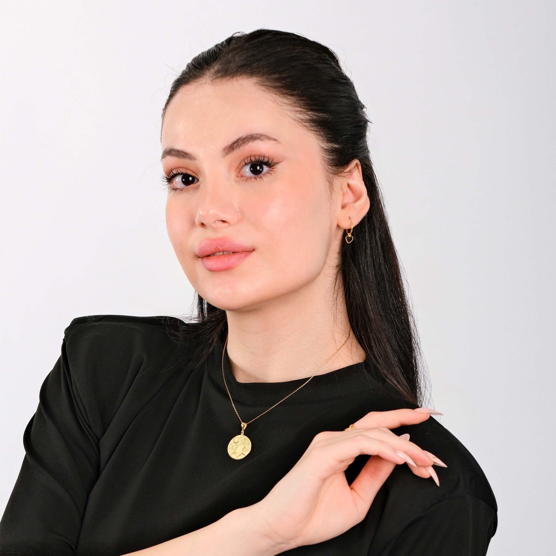 Woman in black top with gold jewelry against white background, showcasing elegant fashion style and accessories.