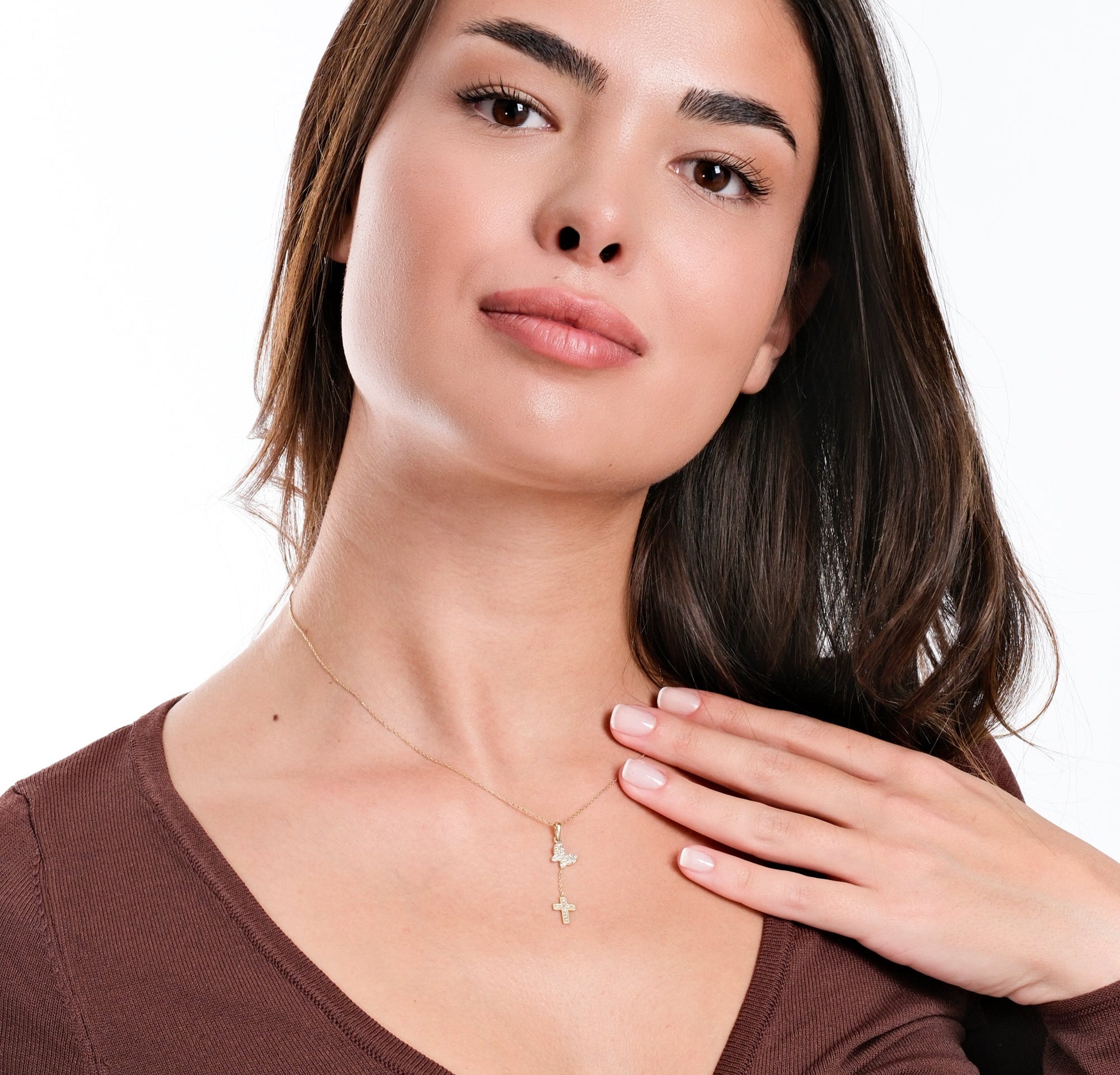 Woman wearing elegant gold necklace with cross and butterfly pendants, brown top, touching collarbone.