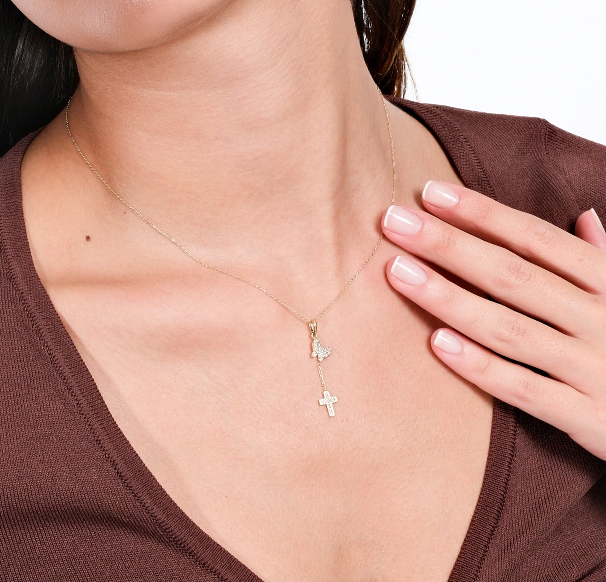 Close-up of woman wearing elegant gold necklace with cross and butterfly pendants, touching her chest.