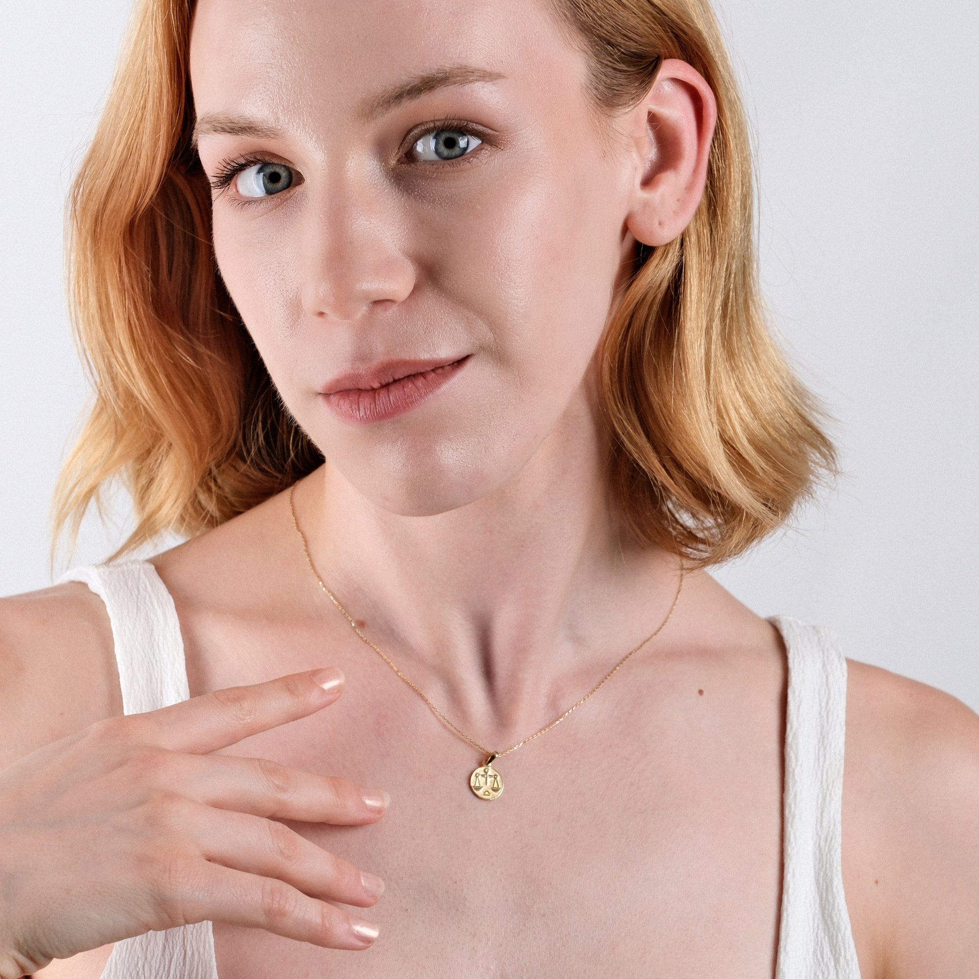Woman wearing a delicate gold necklace with a zodiac pendant, showcasing fashionable jewelry style.