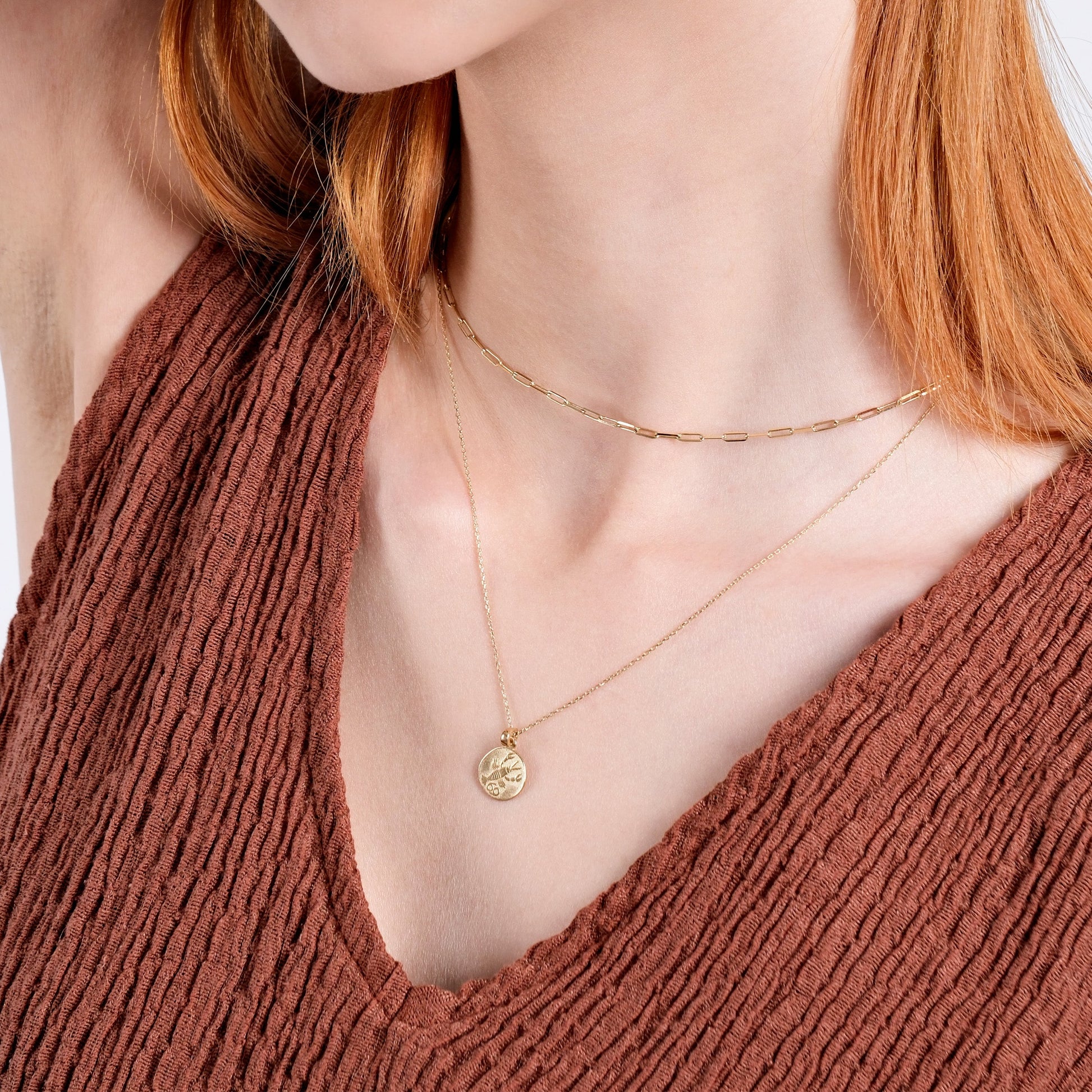 Woman wearing layered gold necklaces with a textured brown top, showcasing elegant minimalist jewelry style.
