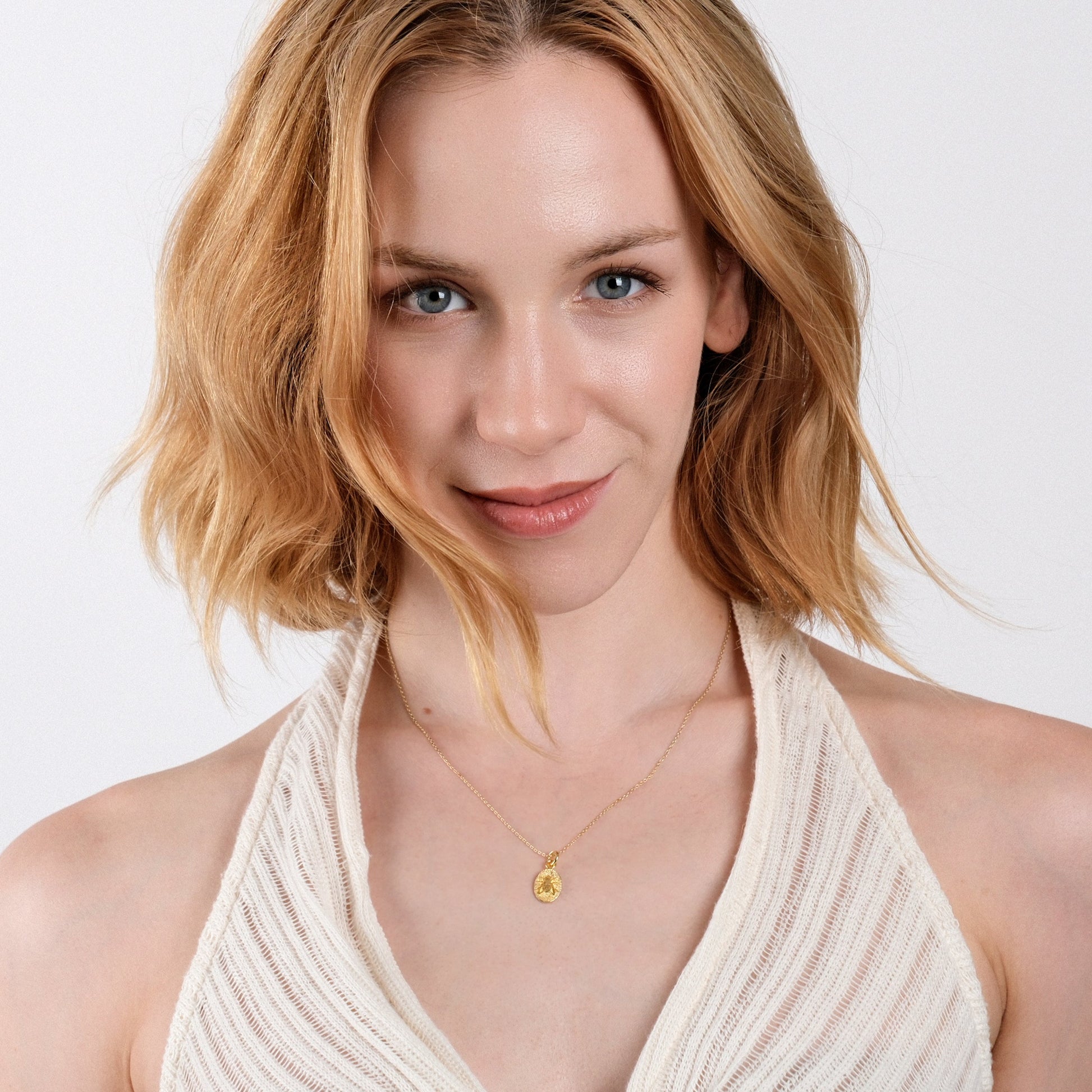 Smiling woman with blonde hair, wearing a gold necklace and white top, isolated on a white background.
