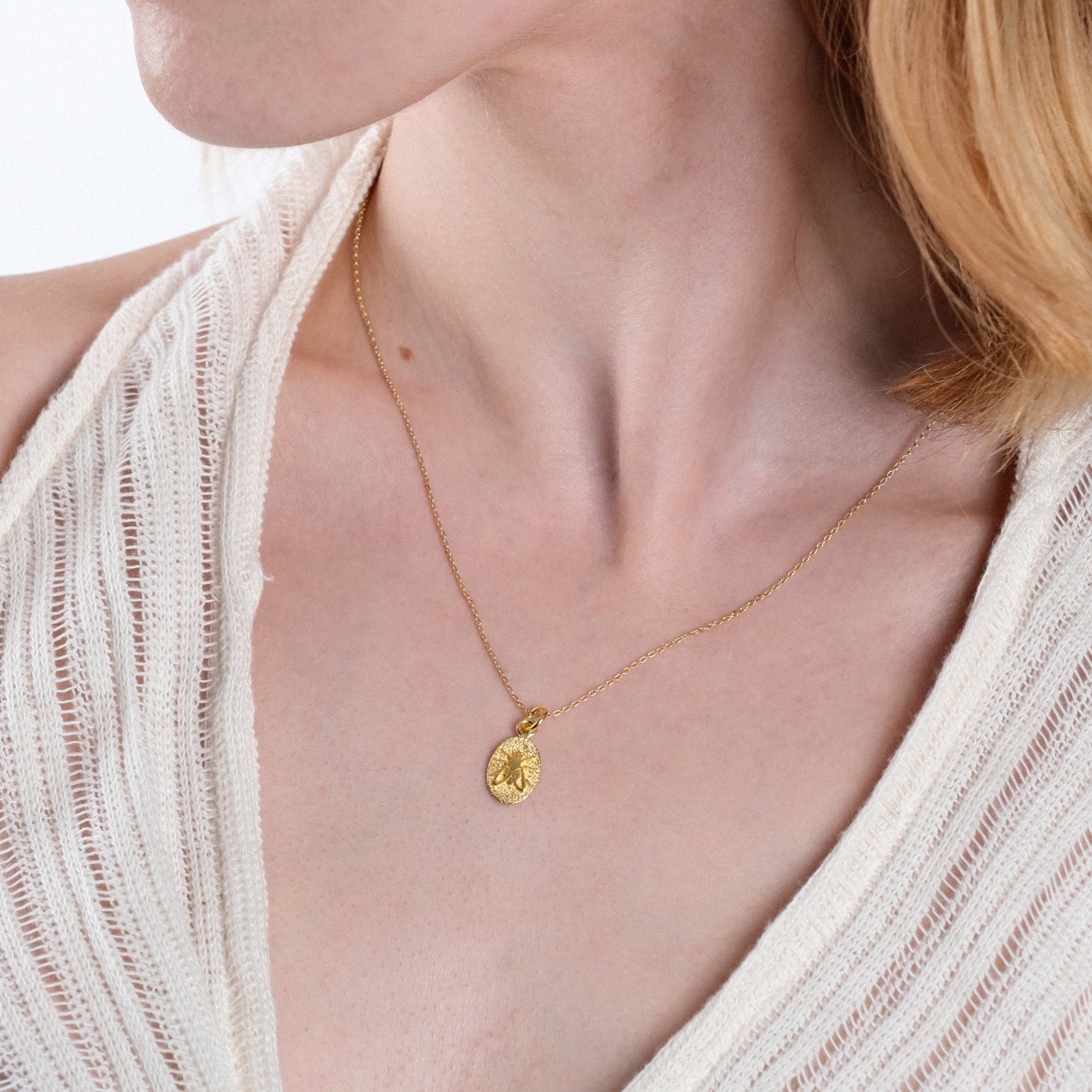 Elegant gold pendant necklace on woman wearing textured white fabric, close-up fashion accessory shot.