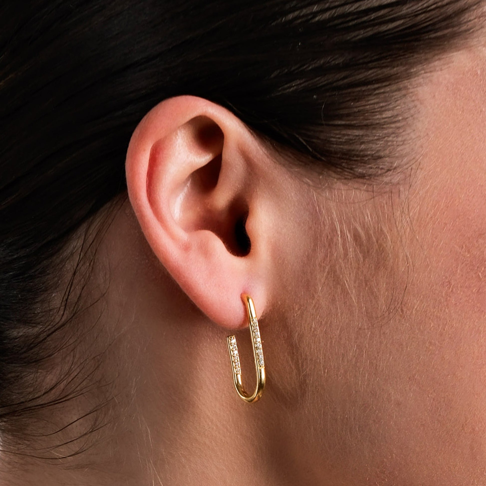 Close-up view of a stylish gold U-shaped hoop earring adorned with sparkling cubic zirconia details. This modern and elegant design adds a touch of sophistication to any look, making it a perfect accessory for both everyday wear and special occasions.