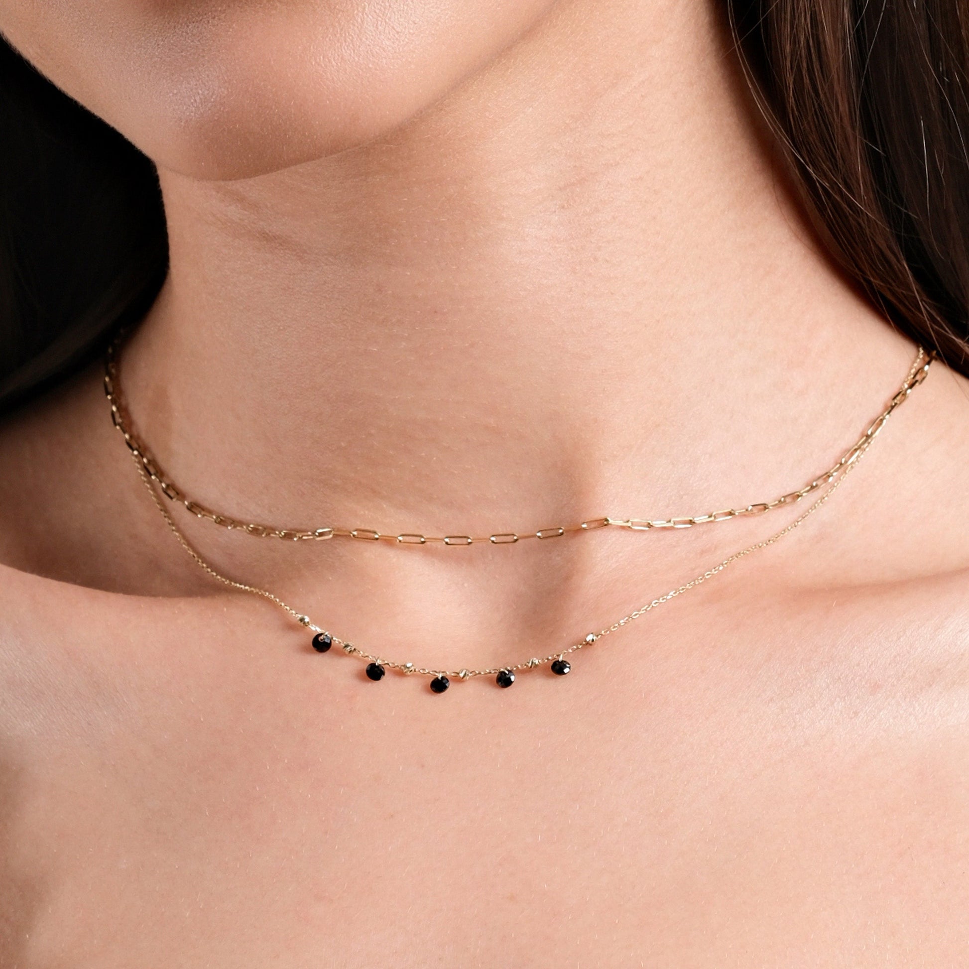 Elegant layered gold necklaces with black gemstone accents on a woman's neck. Perfect jewelry for any occasion.