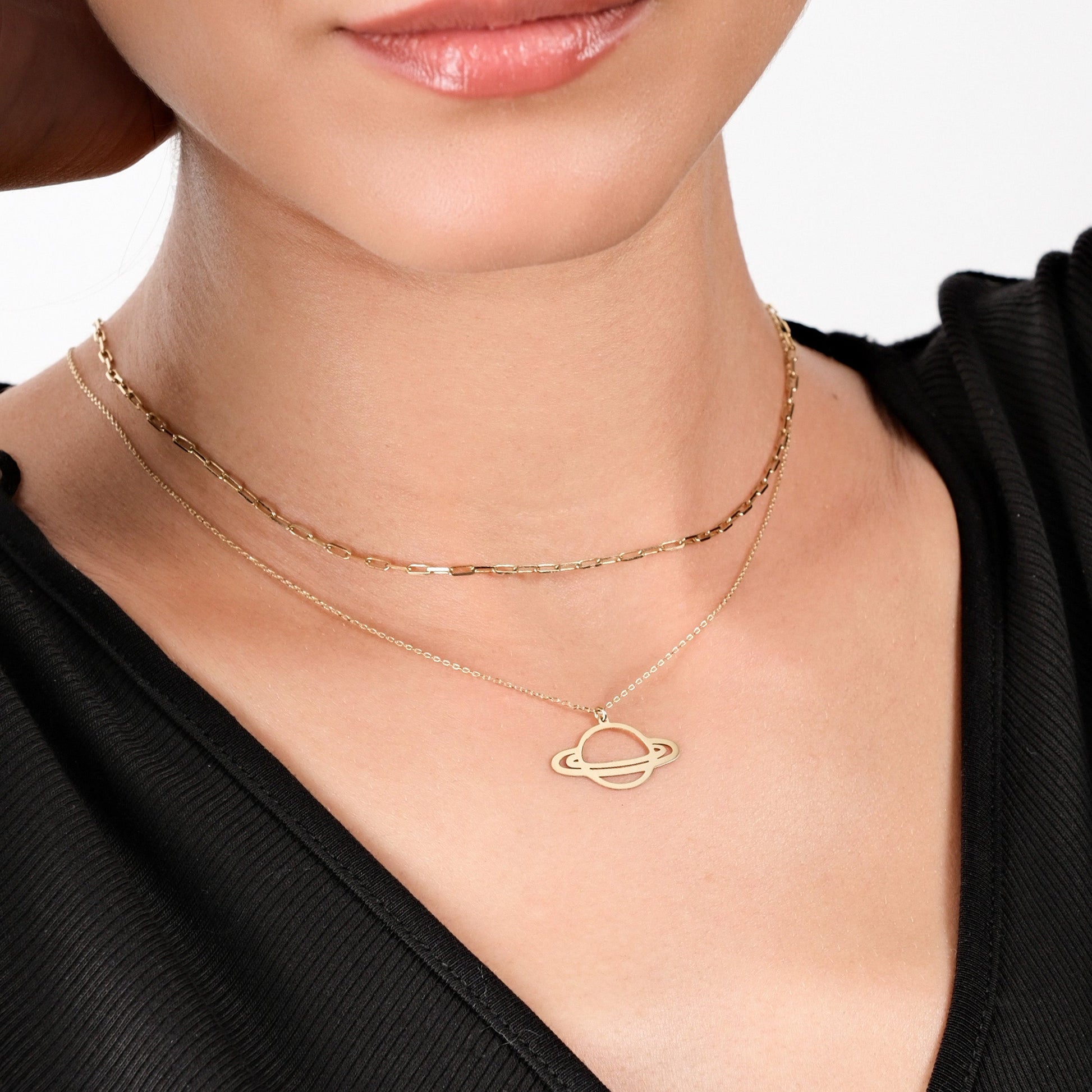 Woman wearing layered gold necklaces with planet pendant, black top background. Fashion jewelry elegance close-up.
