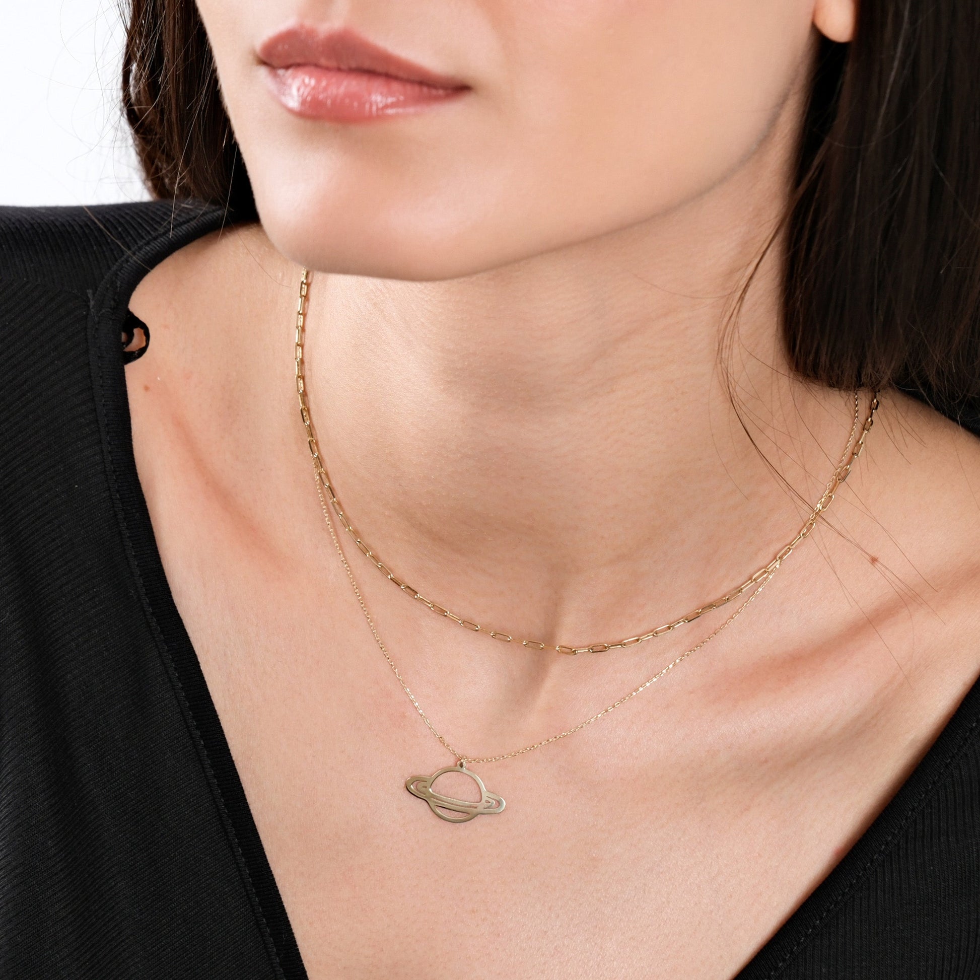 Woman wearing layered gold necklaces with planet pendant, black top, and natural makeup.
