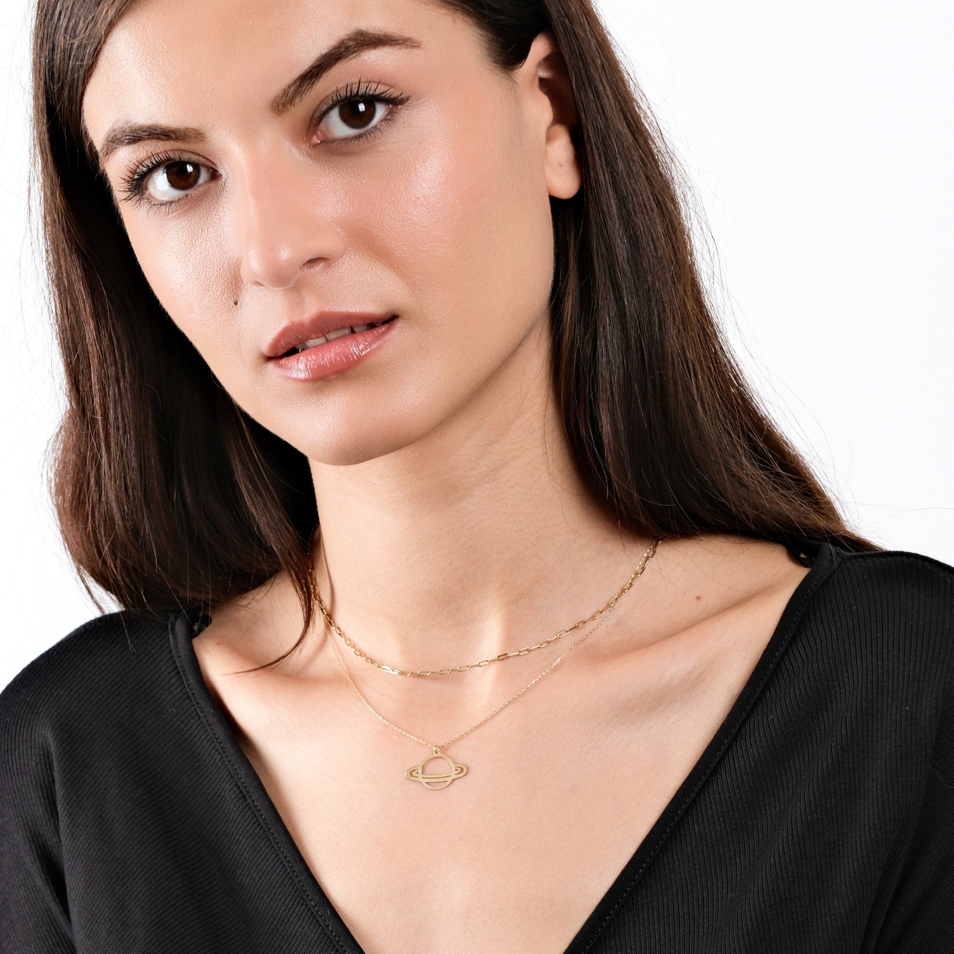 Woman wearing planet necklace, black top, minimal makeup, close-up portrait, elegant style, white background.