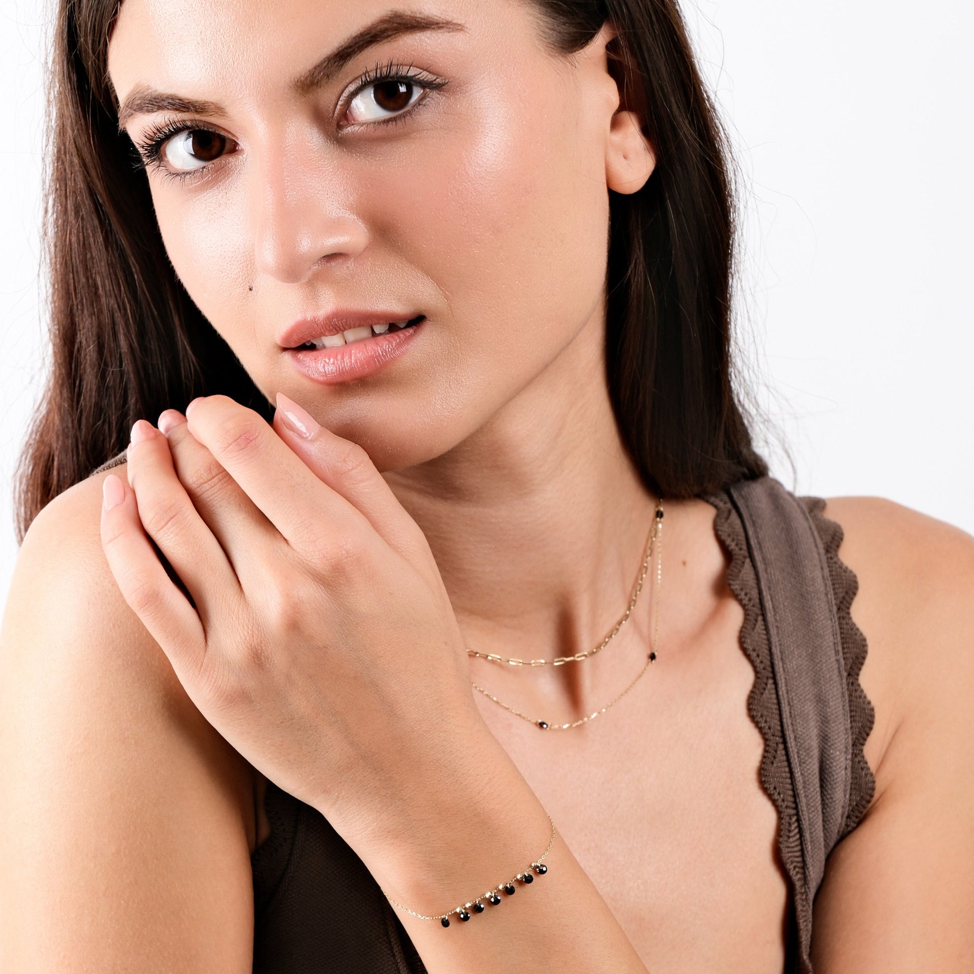 Woman wearing elegant gold jewelry set with black beads, showcasing necklace and bracelet.