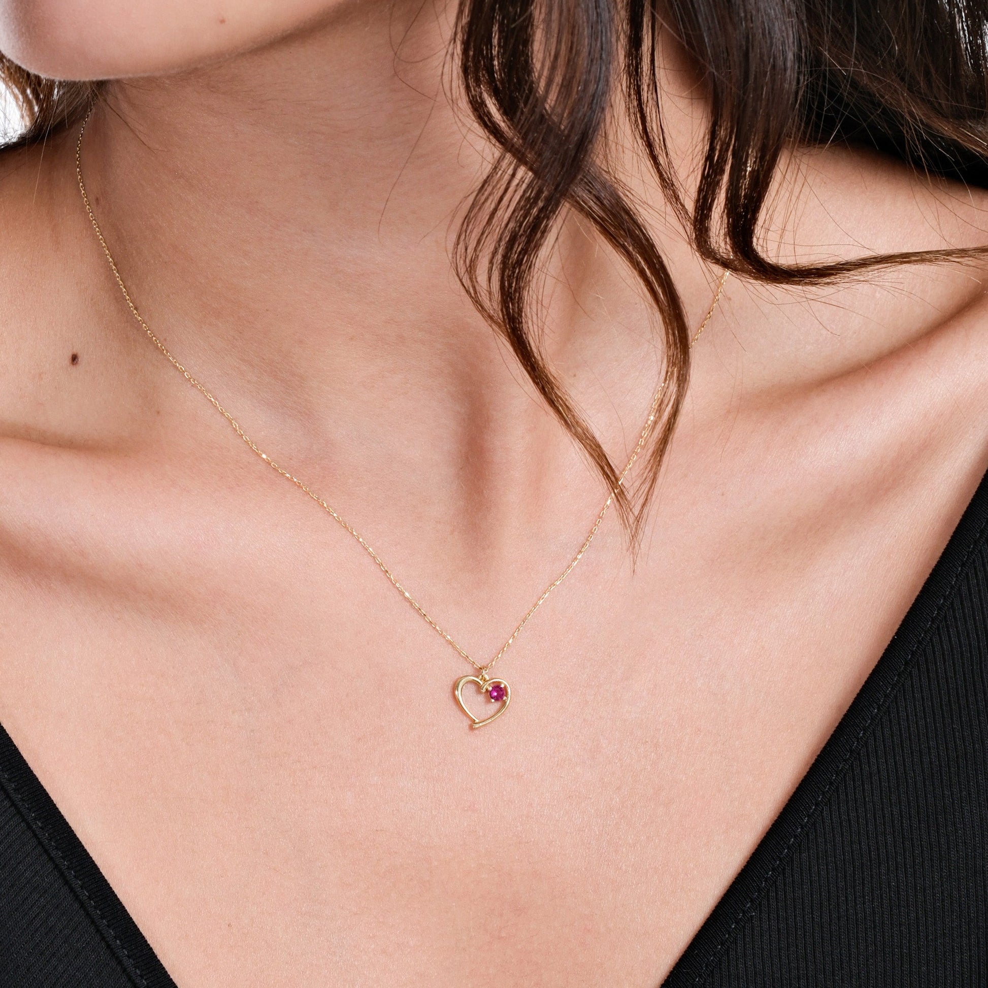 Elegant gold heart necklace with pink gemstone pendant on woman's neck, wearing black top. Perfect for romantic gifts.