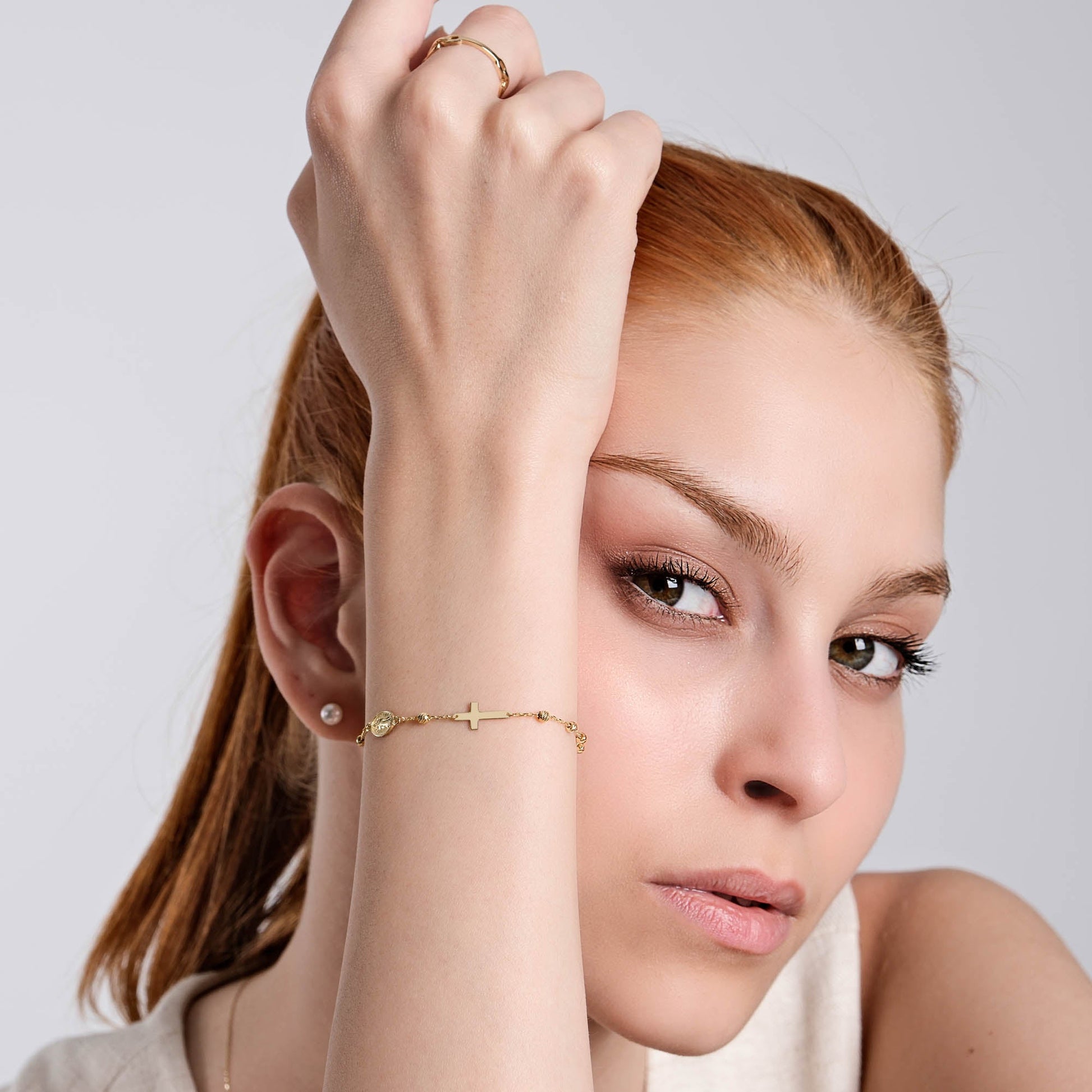 Woman showcasing elegant gold bracelet and ring, highlighting minimalist jewelry style against neutral background.