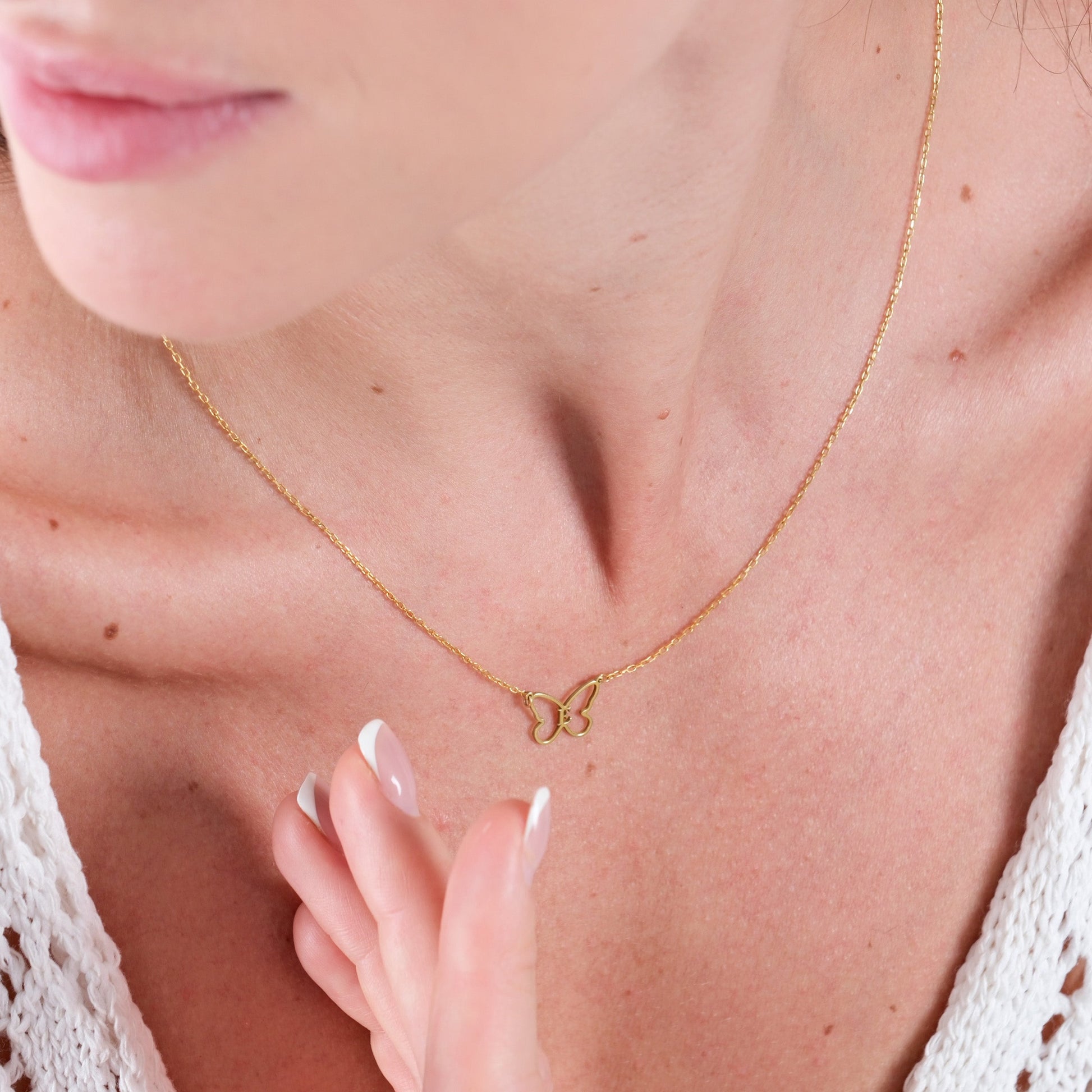 Close-up of woman wearing delicate gold butterfly necklace, white top, and elegant French manicure.