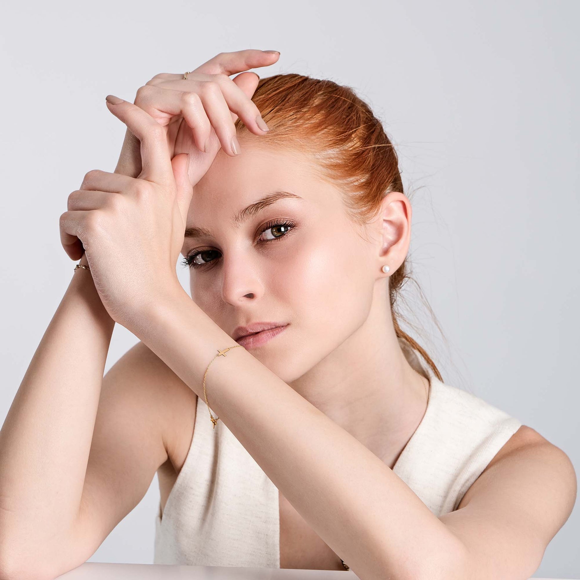 Woman with red hair posing elegantly, wearing minimalist jewelry, against a neutral background.