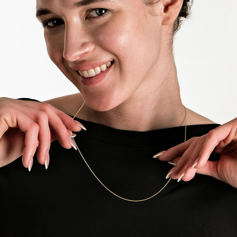 Smiling woman wearing a delicate gold chain necklace against a black top, showcasing elegant fingernail design.