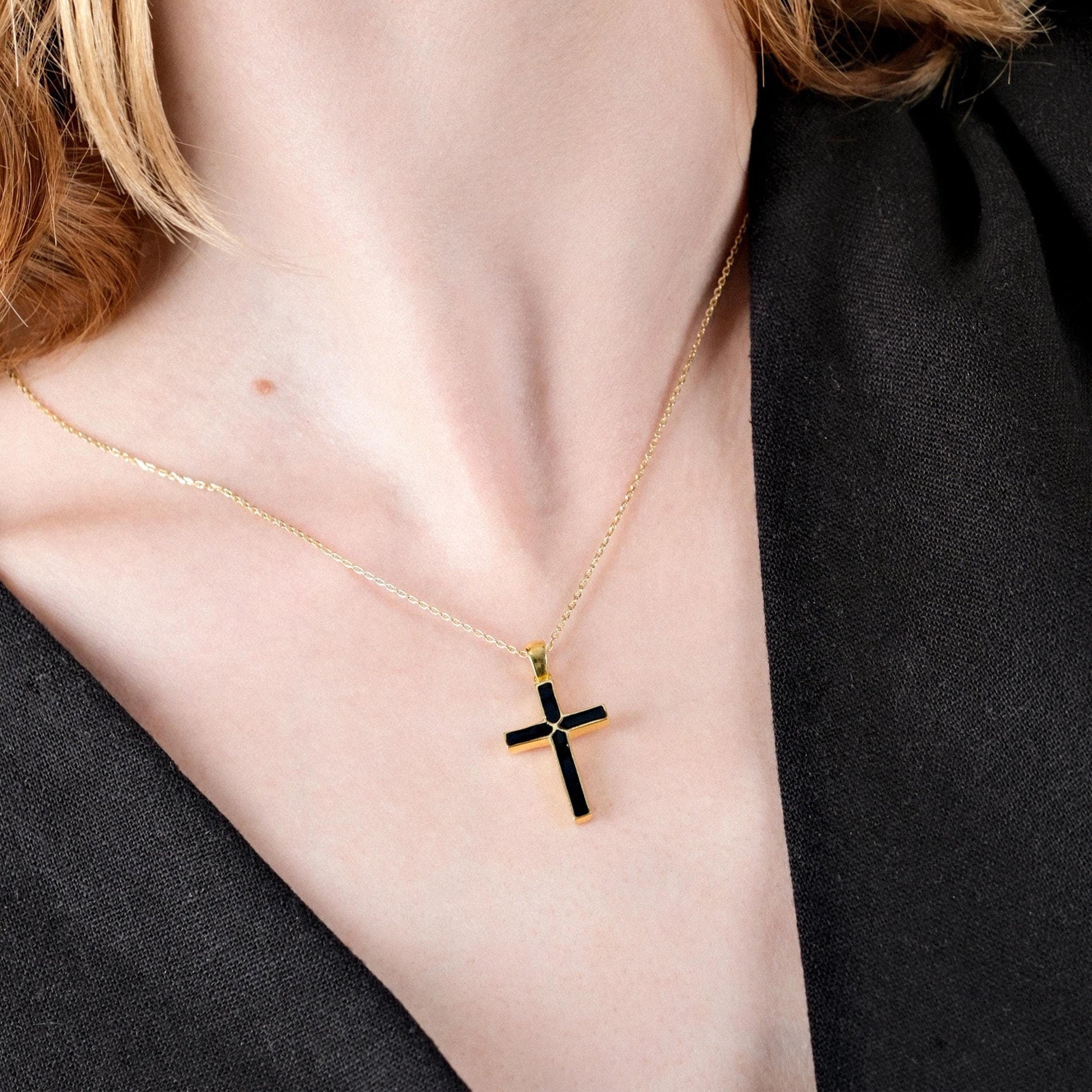 Close-up of a woman's neck, showcasing a 14K gold vermeil necklace with a black cross pendant.