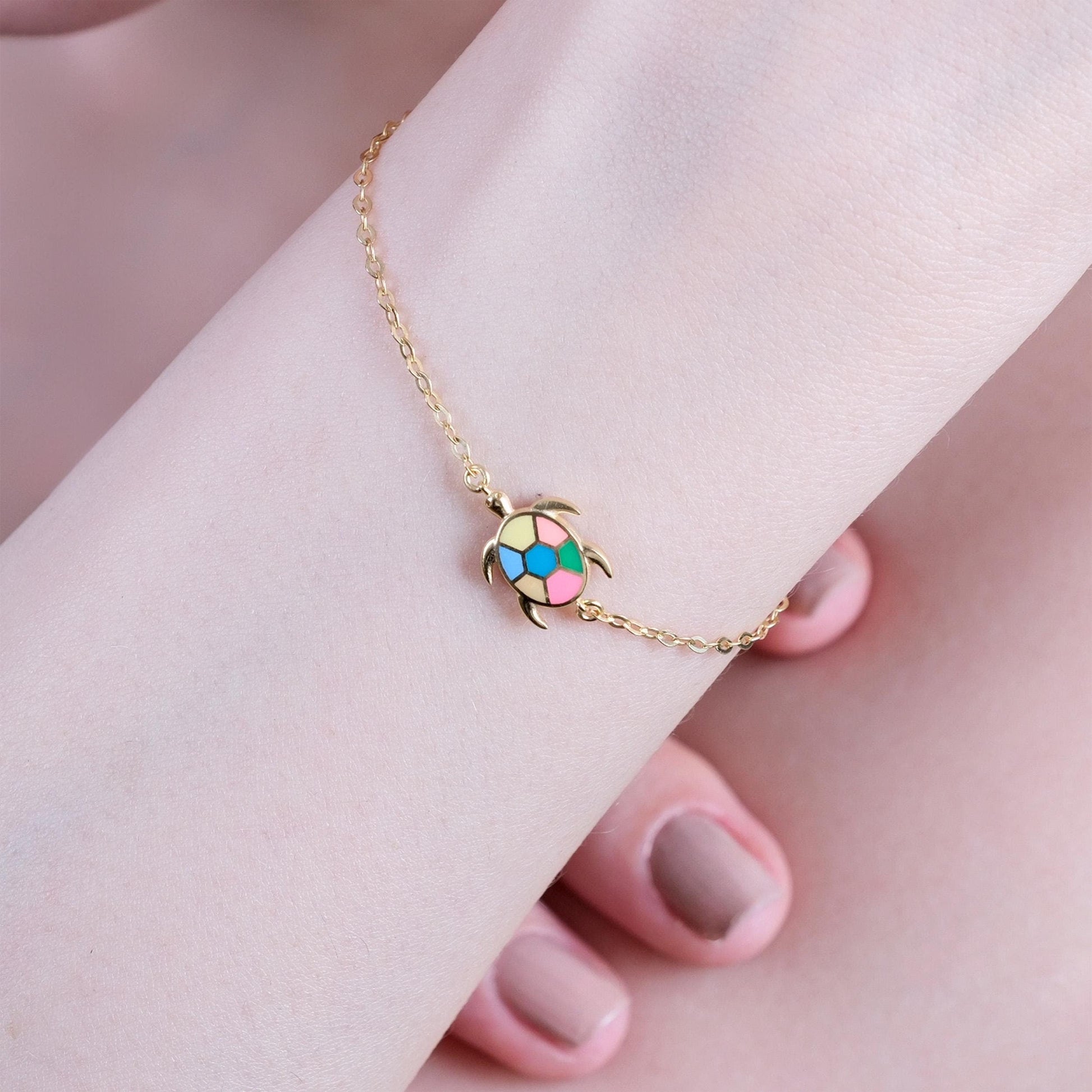 Gold chain bracelet with colorful turtle charm on wrist, showcasing elegant and playful jewelry design.