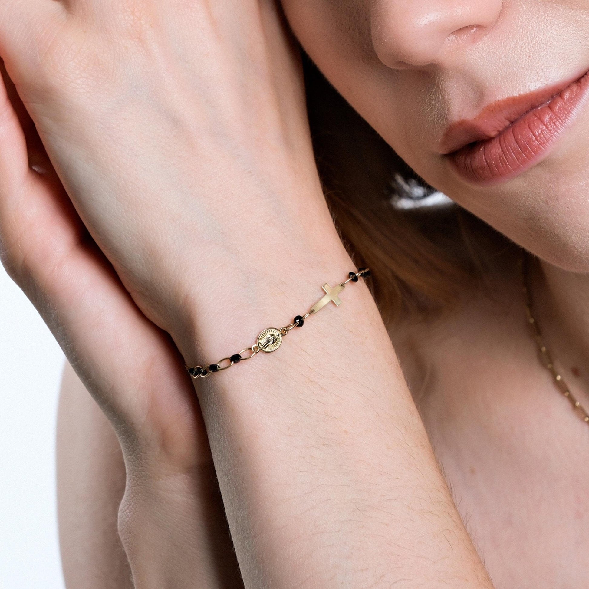 Close-up of a woman's wrist adorned with a delicate 14K solid gold onyx rosary bracelet featuring a small gold cross and medallion charm.