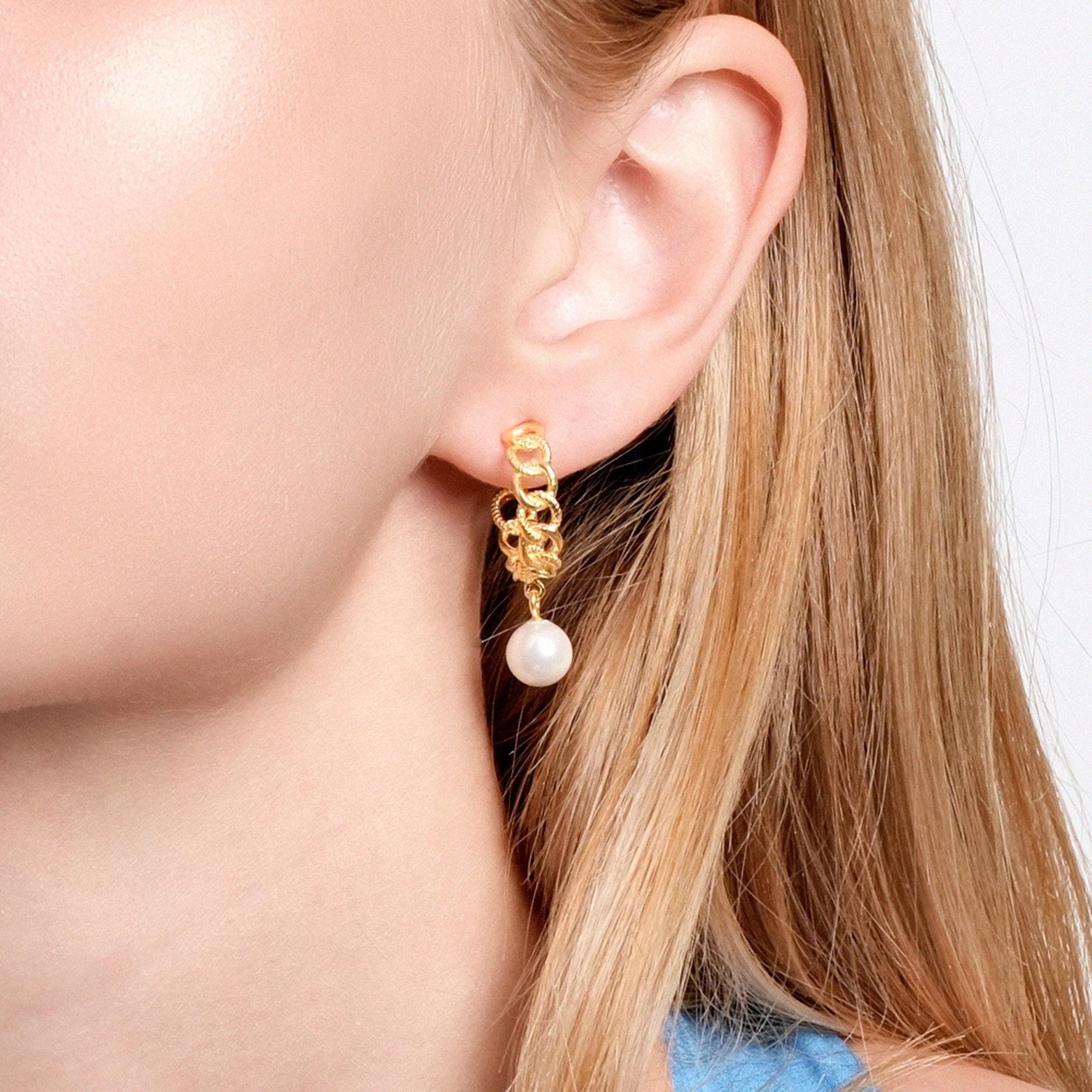 Close-up of a woman's ear wearing a gold hoop earring with a pearl drop.