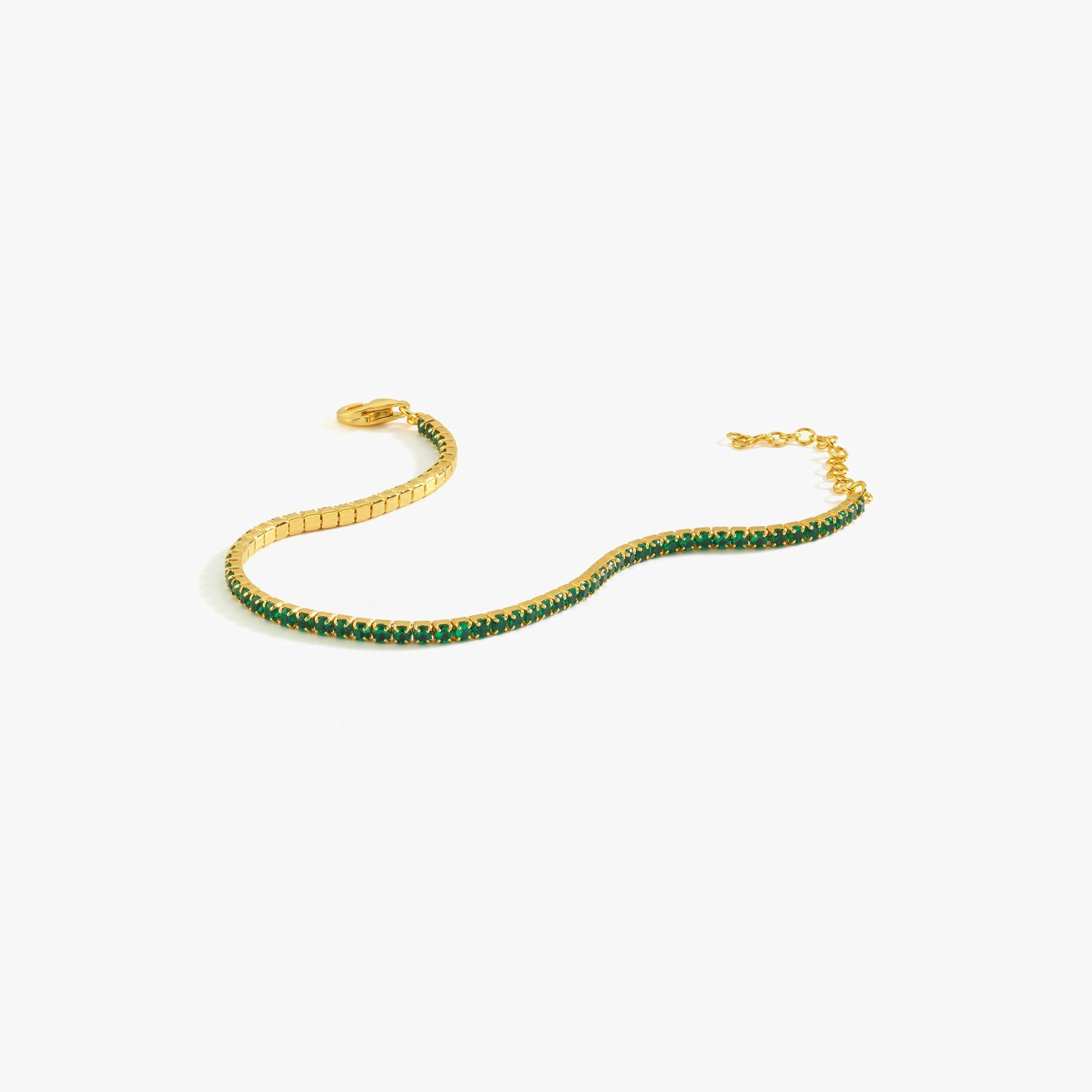 A flat-lay of an 18K gold vermeil emerald tennis bracelet, highlighting its shimmering gold setting and vivid emerald stones.
