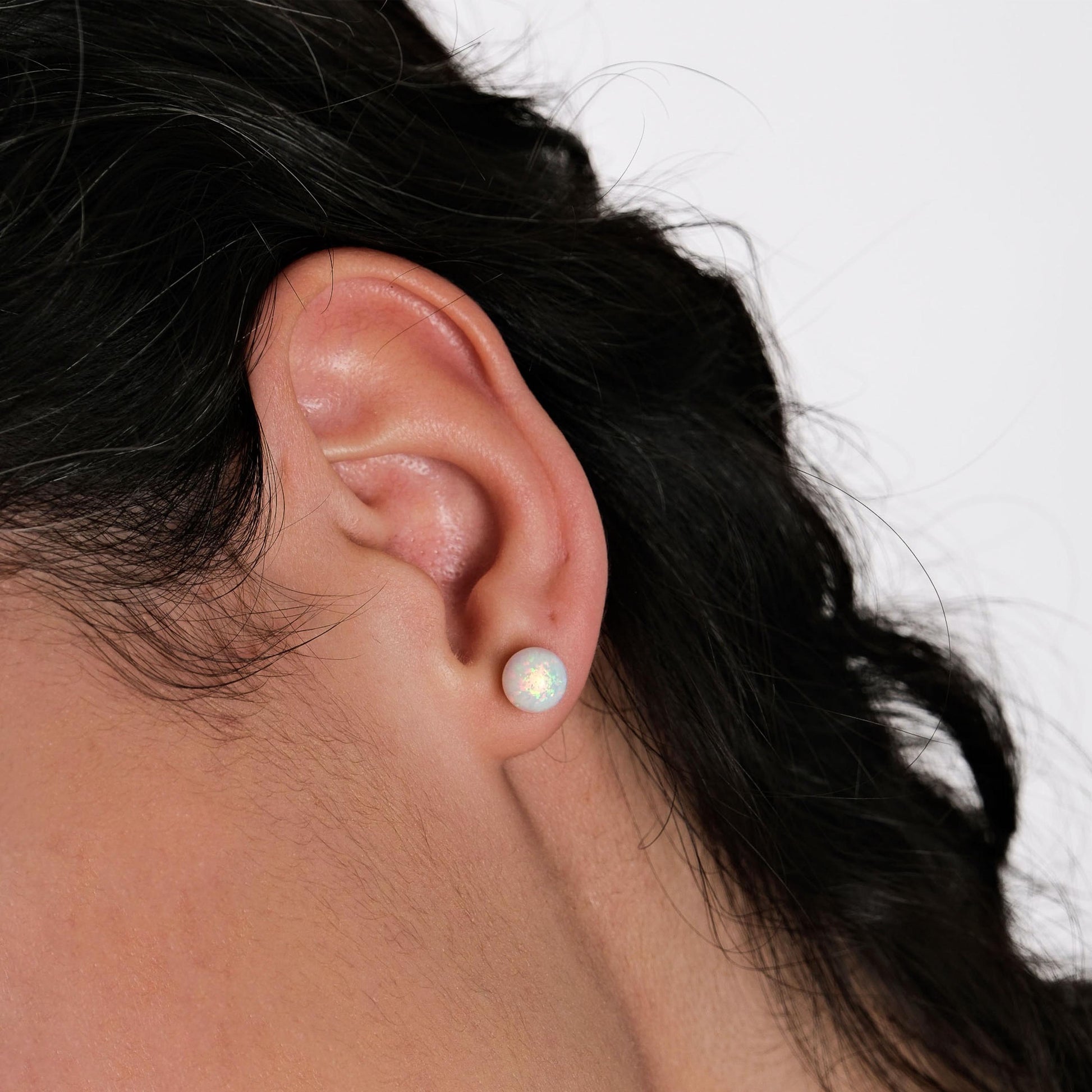 A close-up of an ear adorned with a 14K gold opal stud earring