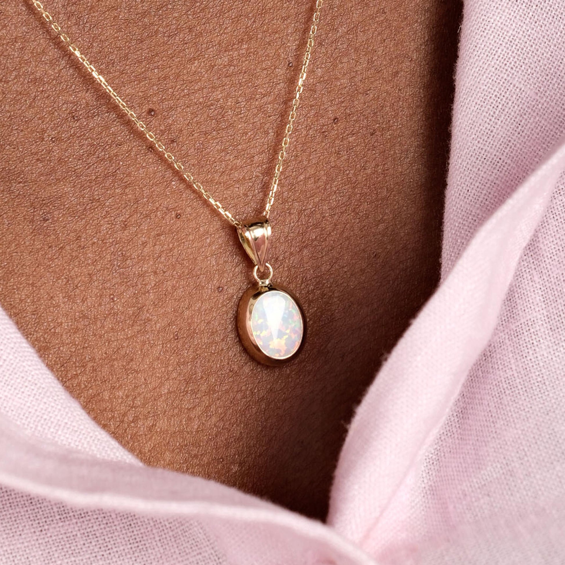 The 14K Solid Gold White Opal Necklace rests on the model’s collarbone, featuring a delicate gold chain and an oval opal pendant.