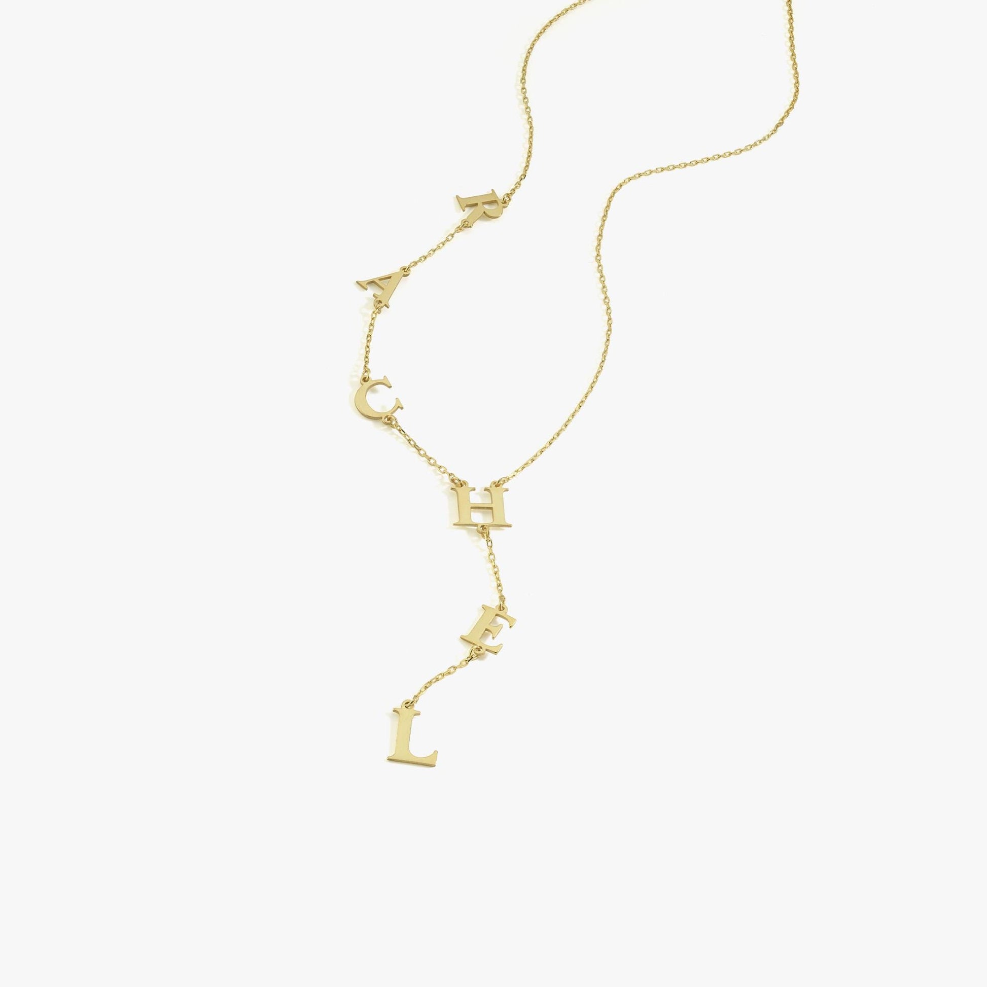 Studio image of a 14K solid gold lariat necklace with dangling letters spelling “RACHEL” against a white background.