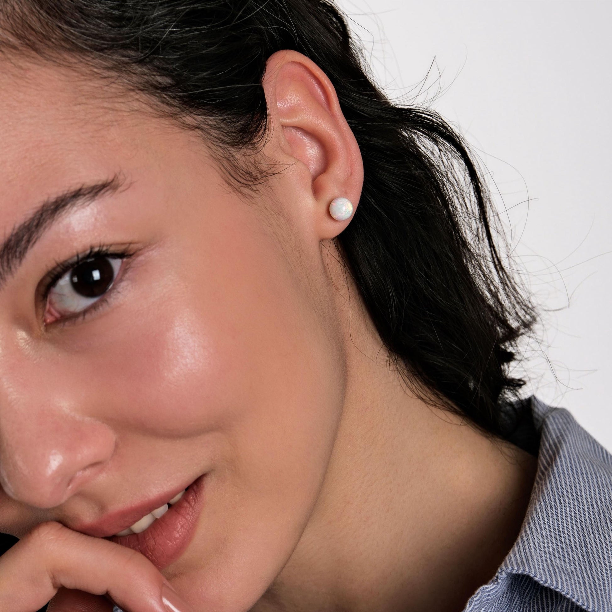 A model playfully resting their chin on their hand, showcasing the subtle beauty of opal stud earrings.