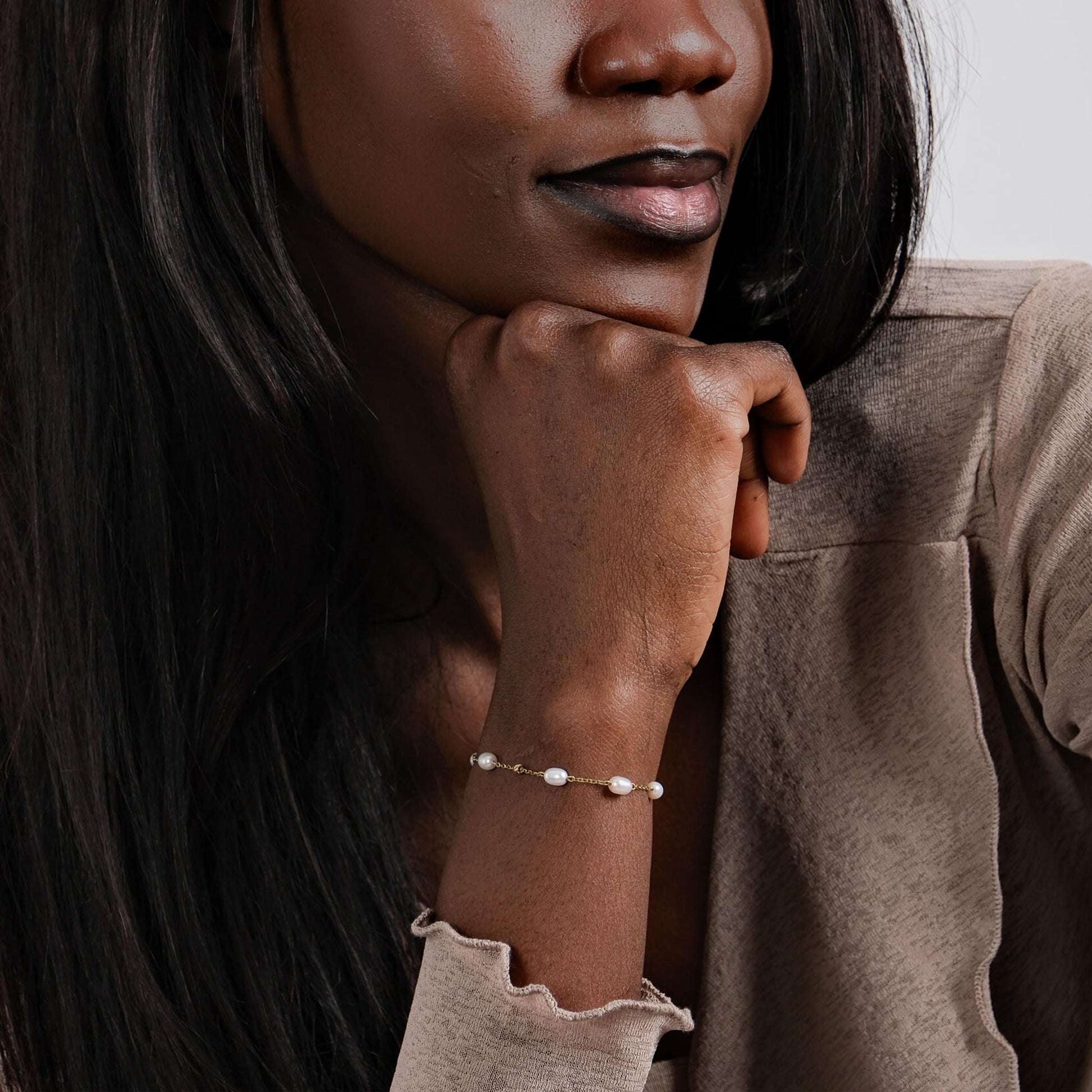 A stylish woman in a beige top gently resting her hand, emphasizing the timeless beauty of the 14K solid gold freshwater pearl bracelet.
