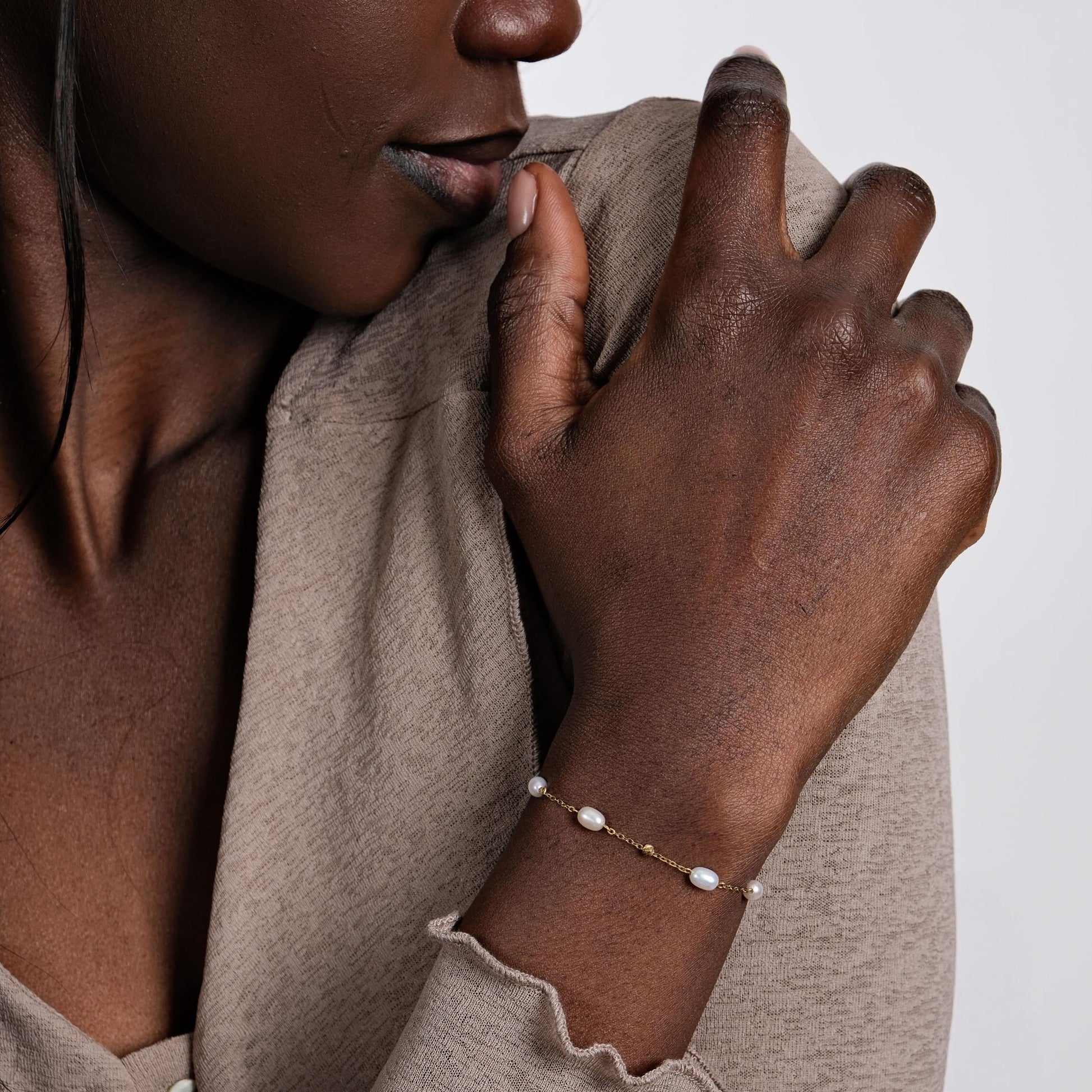 A delicate 14K solid gold freshwater pearl bracelet adorning a model’s wrist, featuring evenly spaced natural pearls on a fine gold chain.