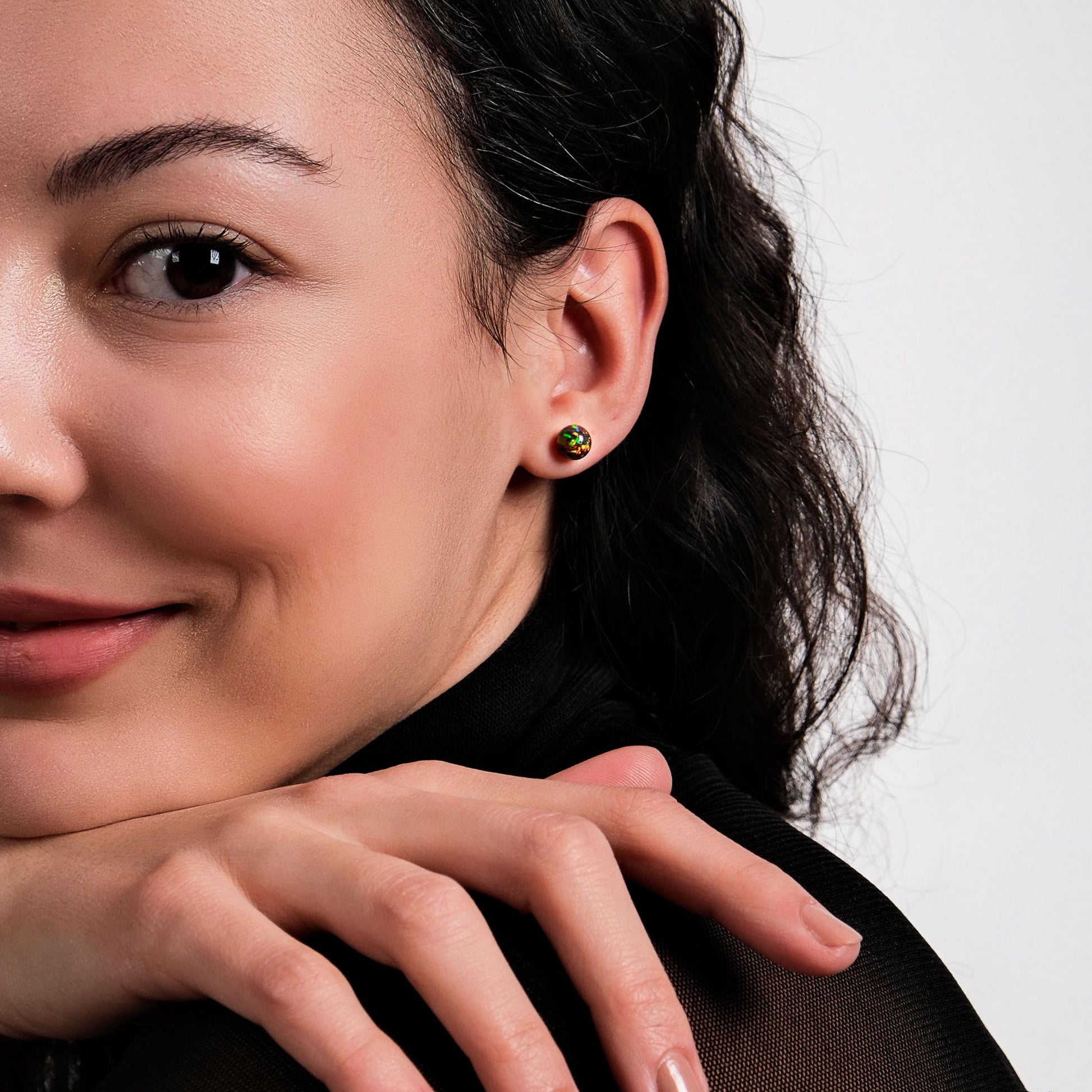 A woman resting her chin on her hands, smiling softly, with fire opal earrings adding a touch of color.