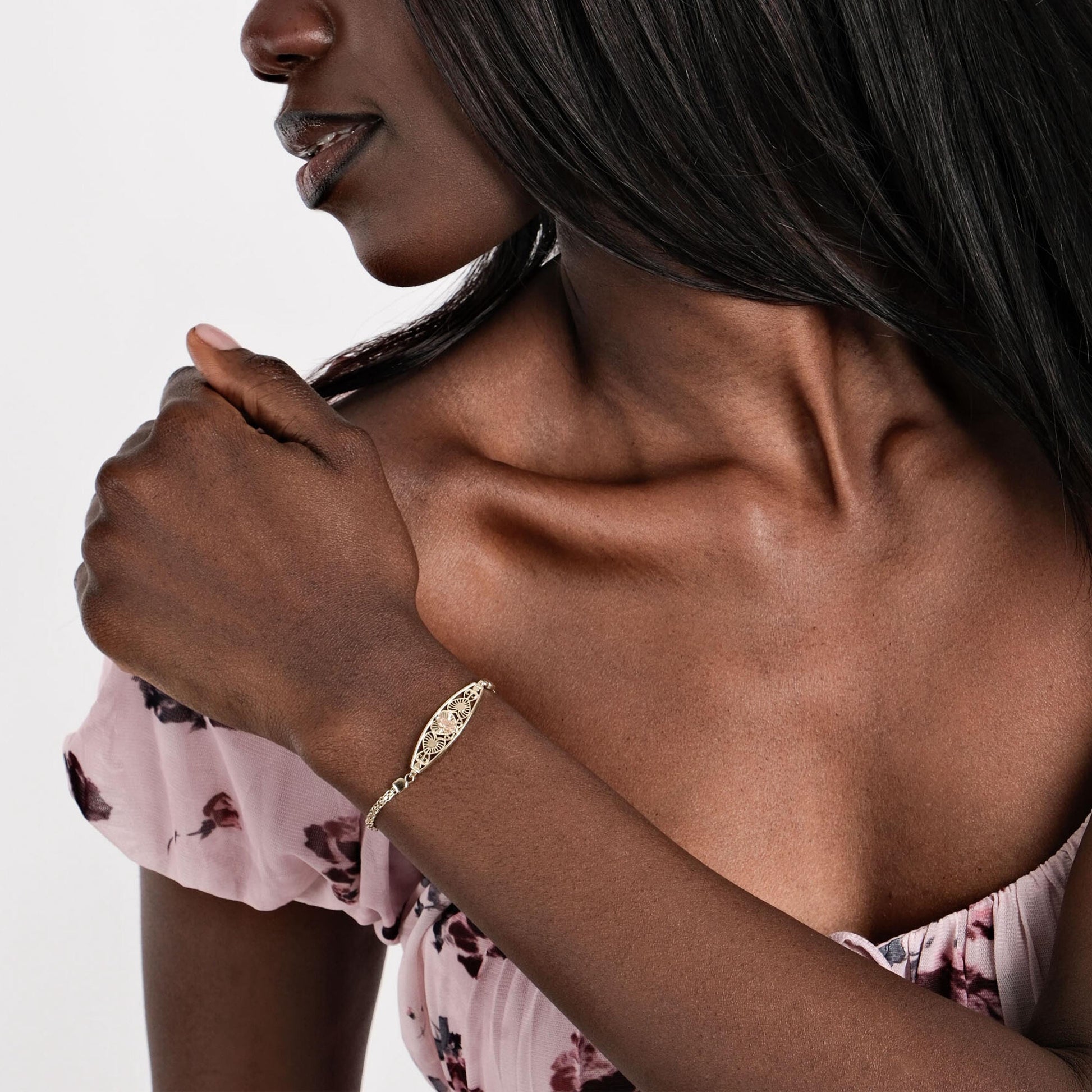 A woman wears a 14K solid gold Virgen de Guadalupe bracelet, pairing it with a floral dress for an elegant look.