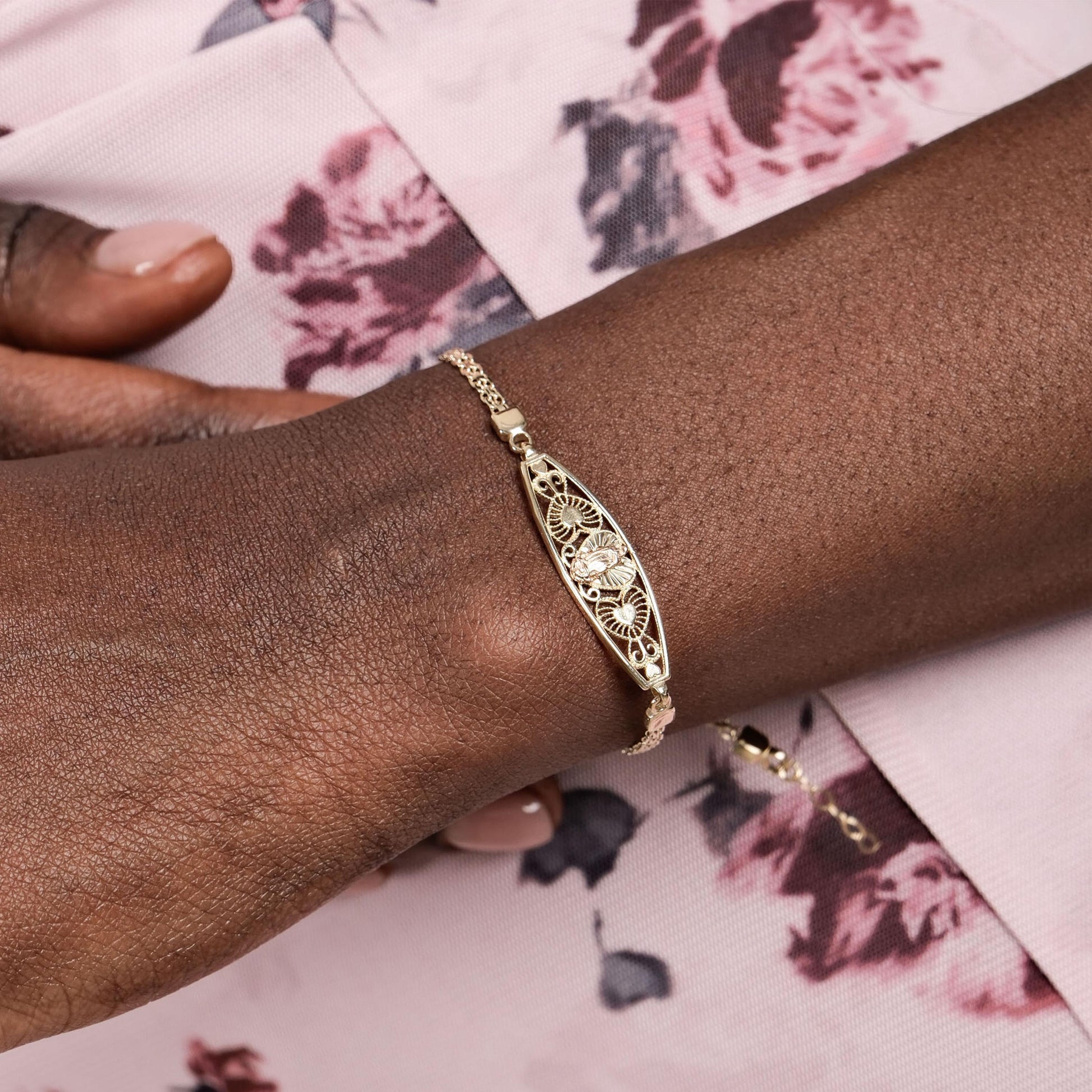 A 14K solid gold Virgen de Guadalupe bracelet with a delicate filigree design worn on a wrist, showcasing its intricate details.
