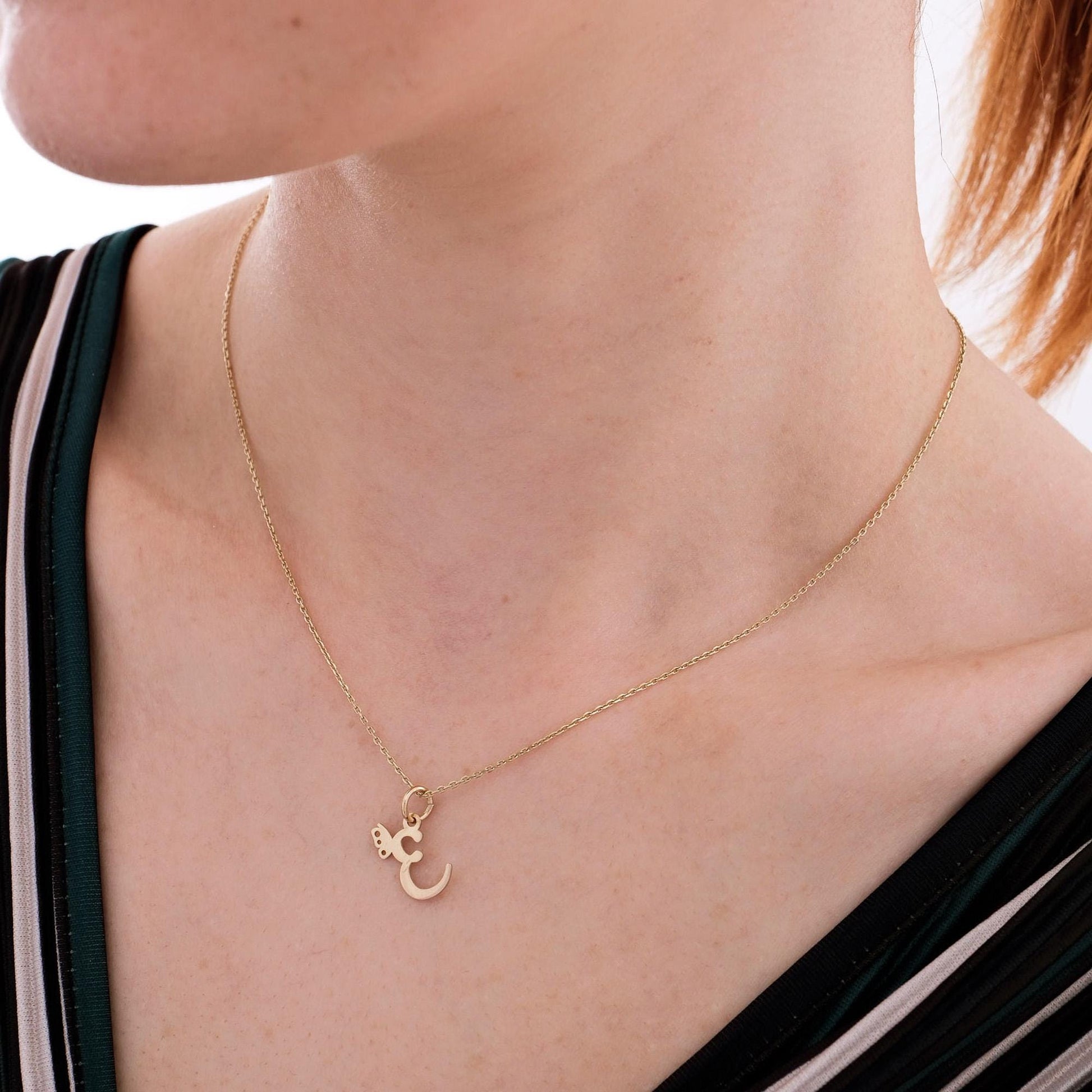 14K solid gold custom letter necklace with butterfly accent, focusing on the engraved "E" pendant on soft fabric.