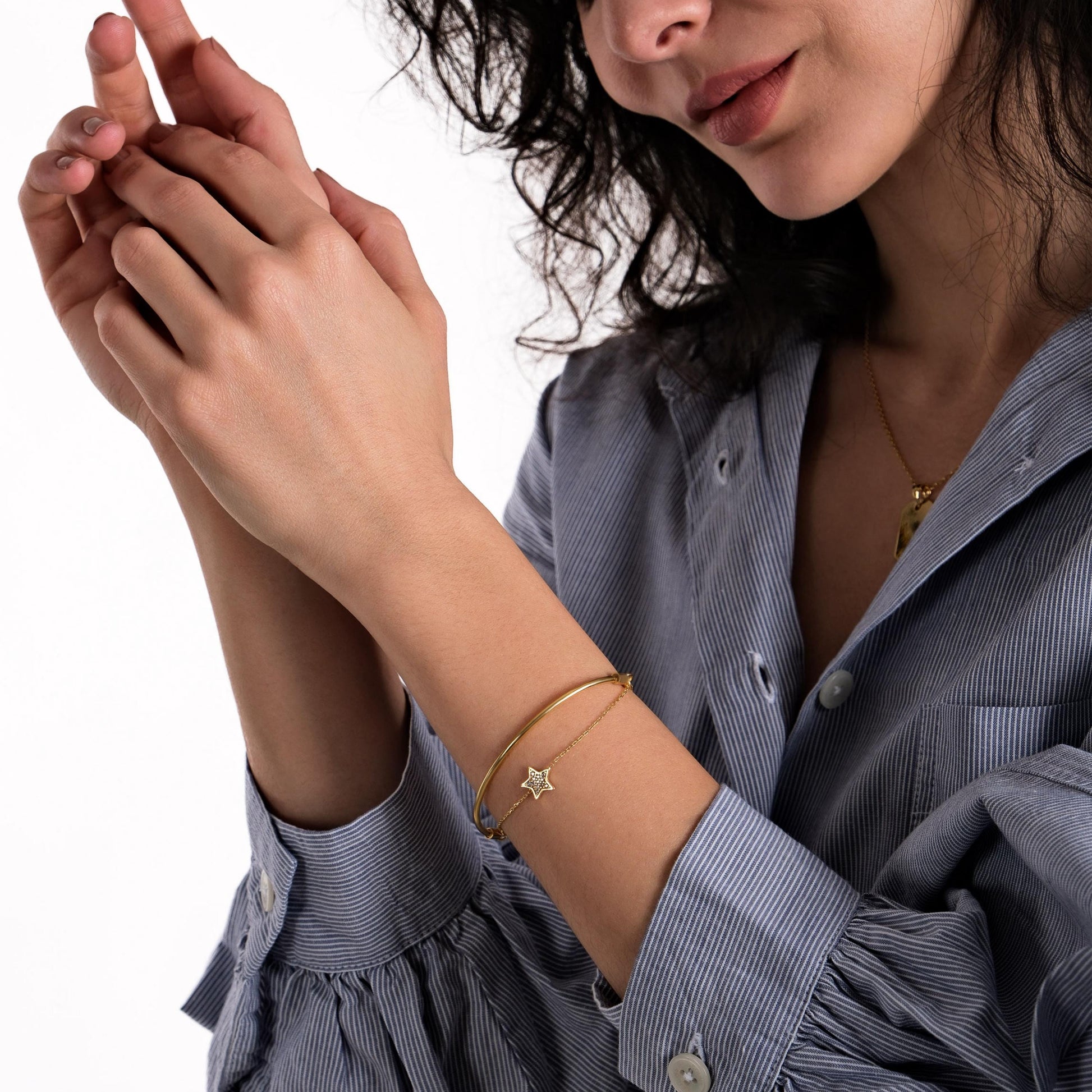 A smiling woman wearing a 18K gold vermeil sliding adjustable bracelet, featuring a star charm, over the sleeve of a blue striped blouse.