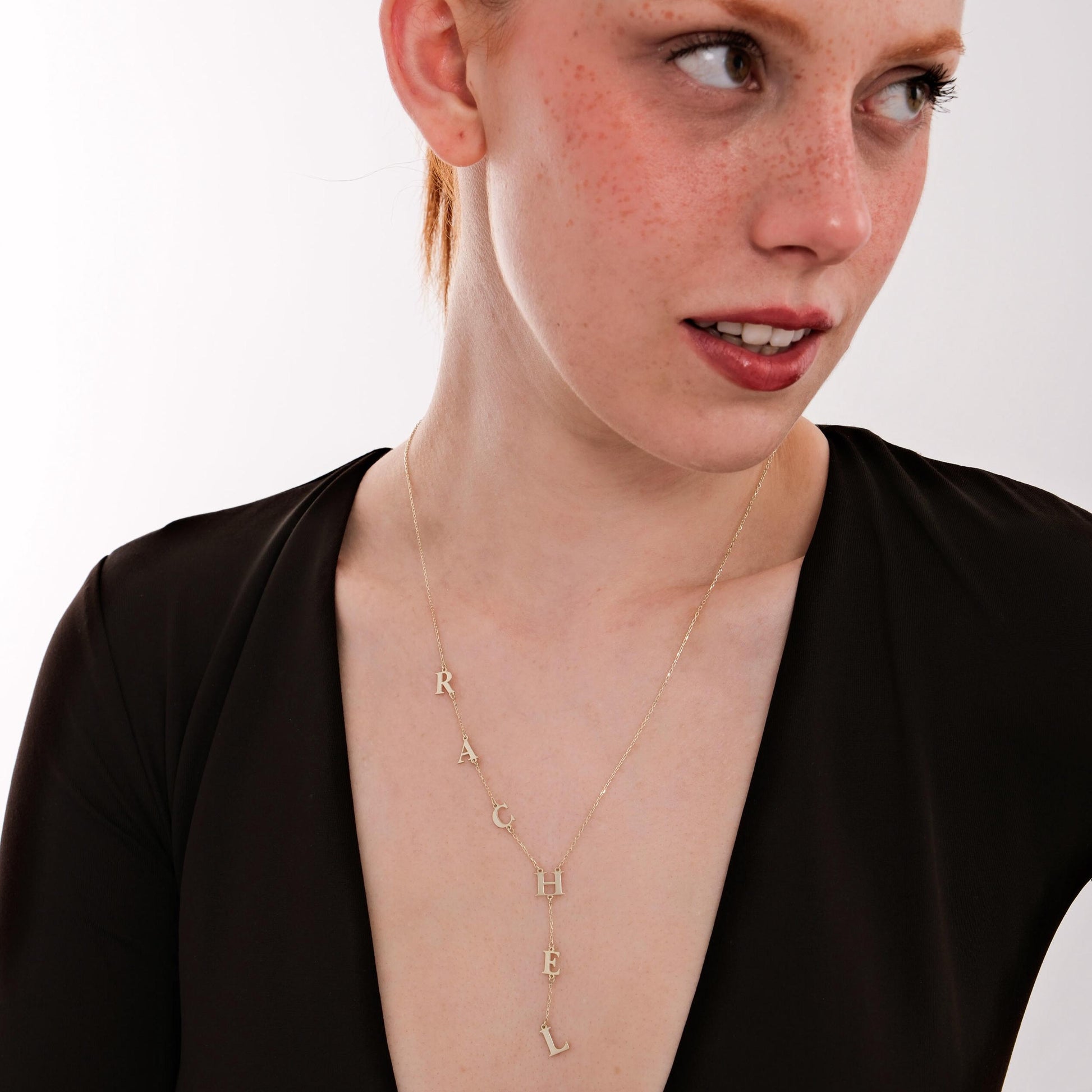 Front-facing image of a woman wearing a delicate 14K solid gold lariat necklace with the name “RACHEL” spelled vertically.
