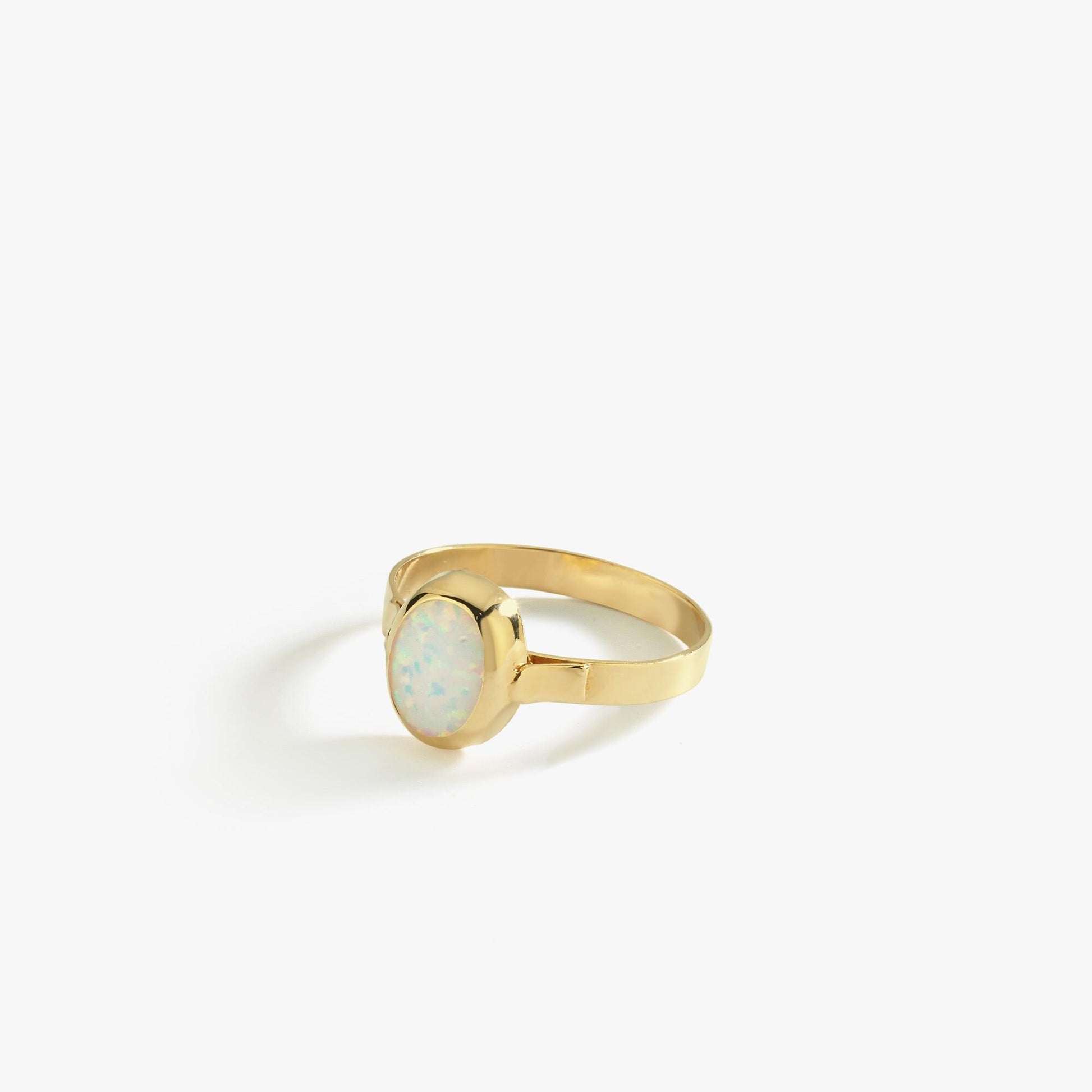 Side view of a 14K solid gold white opal ring with an iridescent oval opal stone, styled in a clean bezel setting on a reflective surface.
