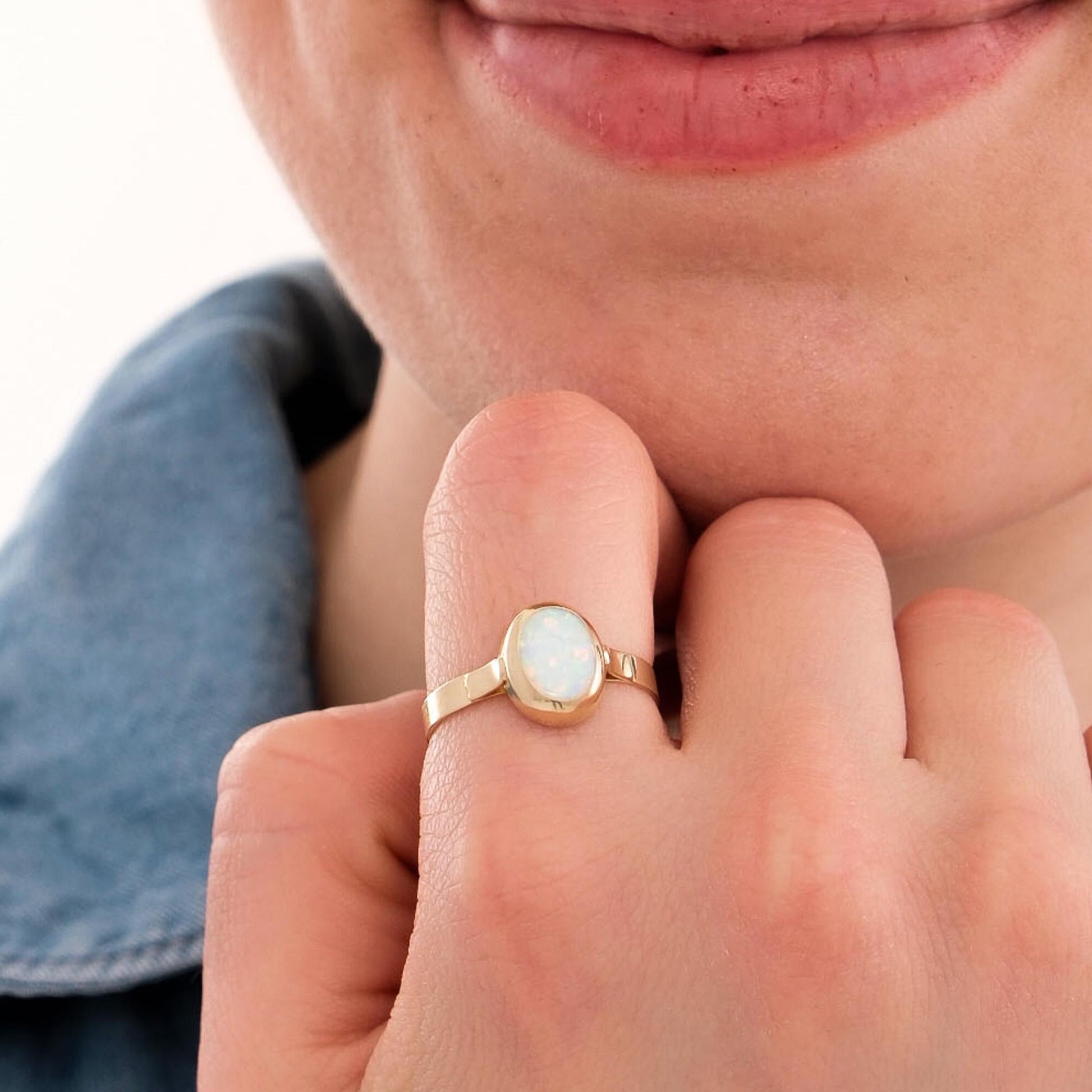 Close-up of a woman gently touching her face, showcasing a 14K solid gold white opal ring with a smooth oval stone and polished band.