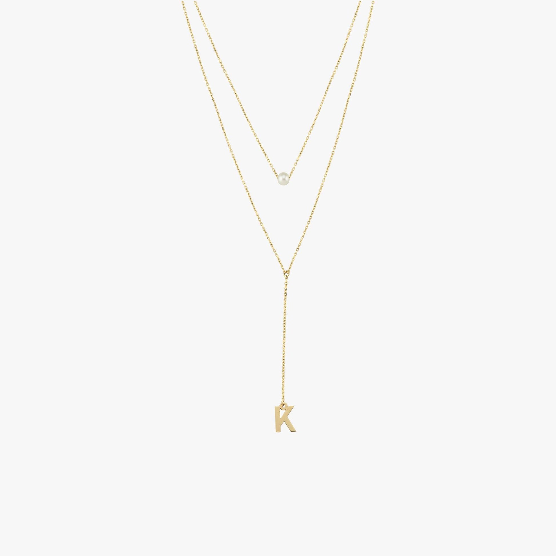 Flat lay of a 14K solid gold pearl lariat necklace featuring a single pearl and a 'K' charm, styled with two fine gold chains.