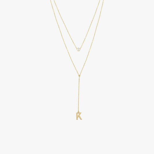 Flat lay of a 14K solid gold pearl lariat necklace featuring a single pearl and a 'K' charm, styled with two fine gold chains.