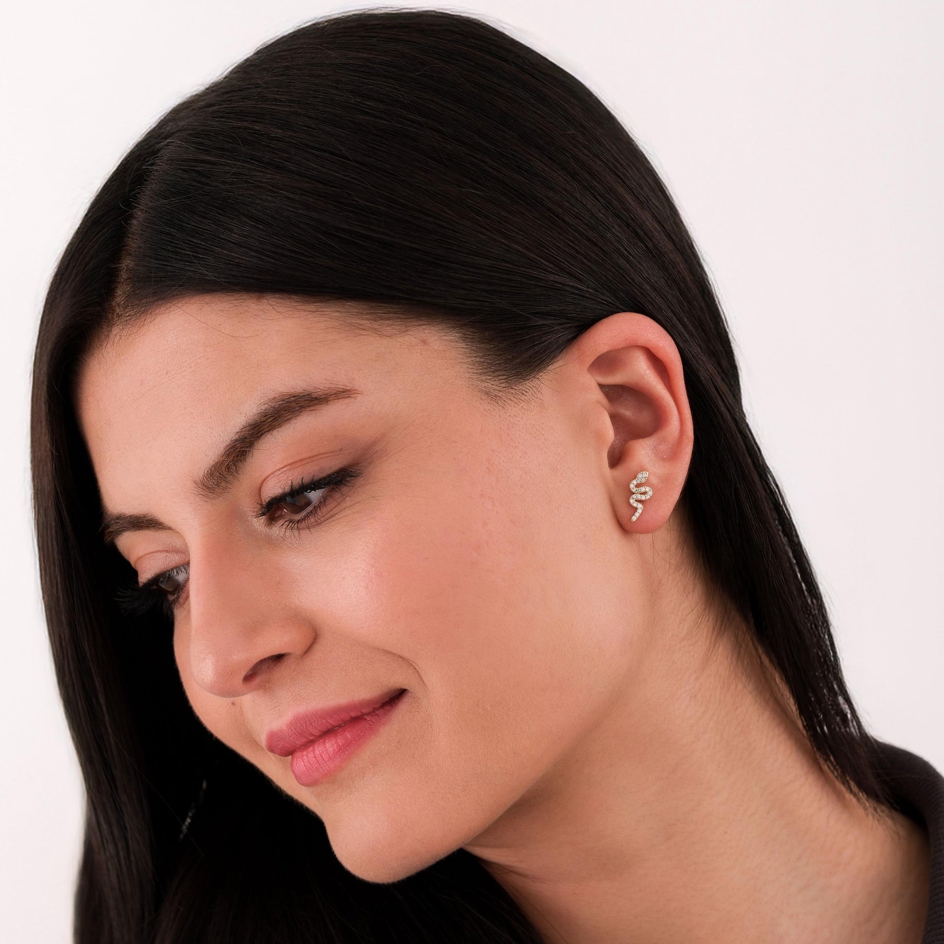 Woman with straight dark hair and minimal makeup wearing a 14K solid gold snake stud earring.