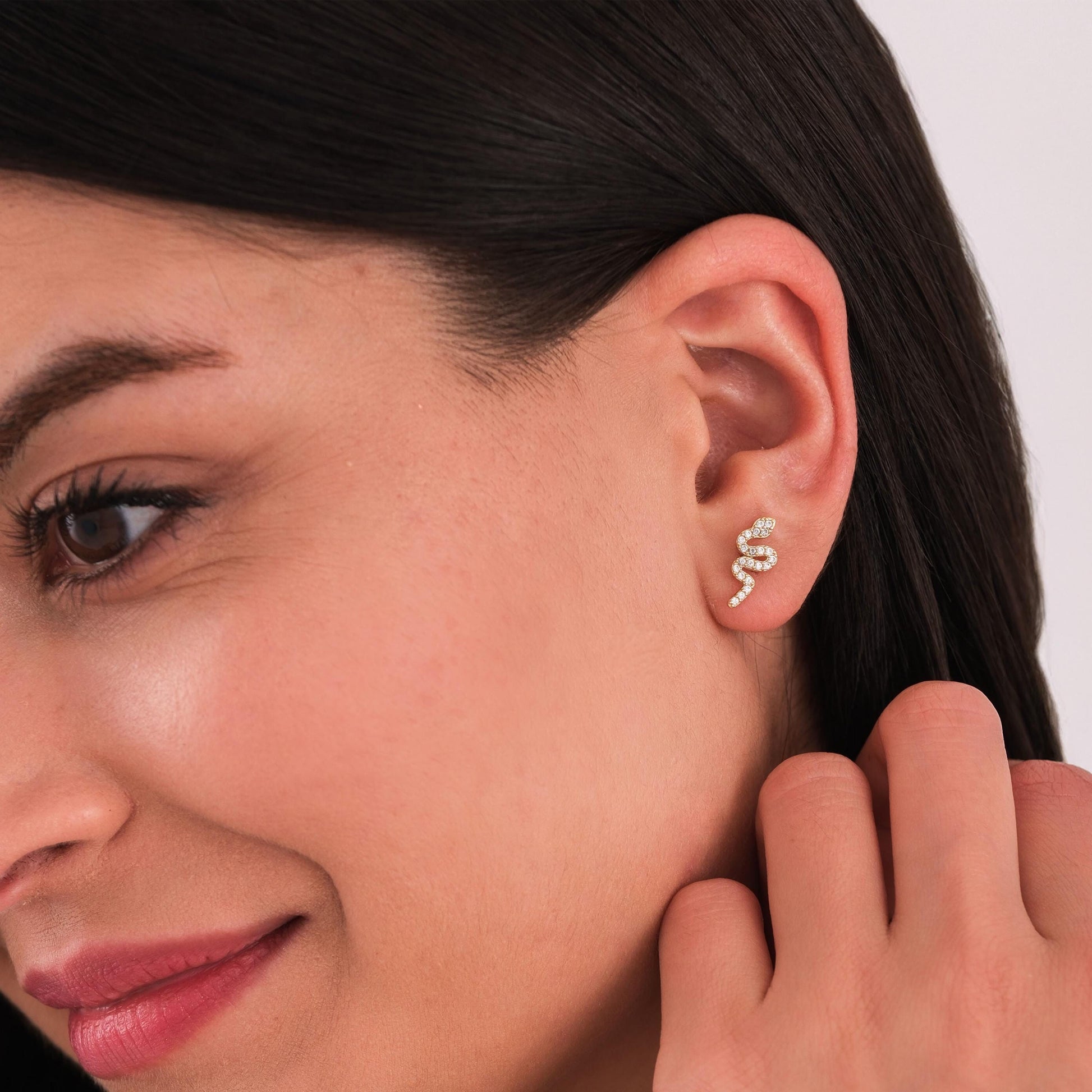 Close-up profile of a woman gently touching her 14K solid gold snake stud earring, styled with a sleek hairstyle.