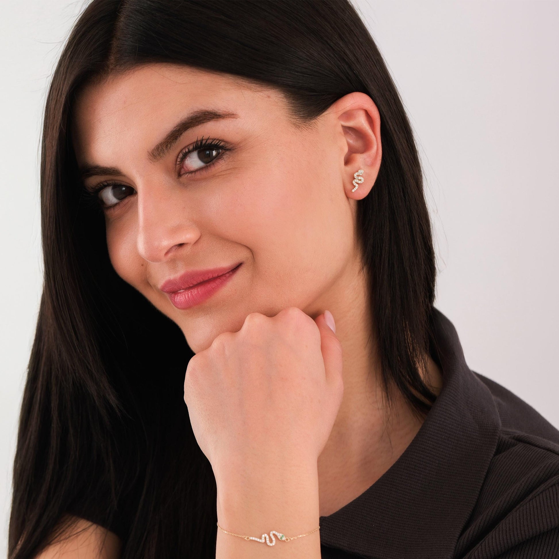 Woman smiling with matching 14K solid gold snake stud earring and bracelet set, styled in a casual black top.