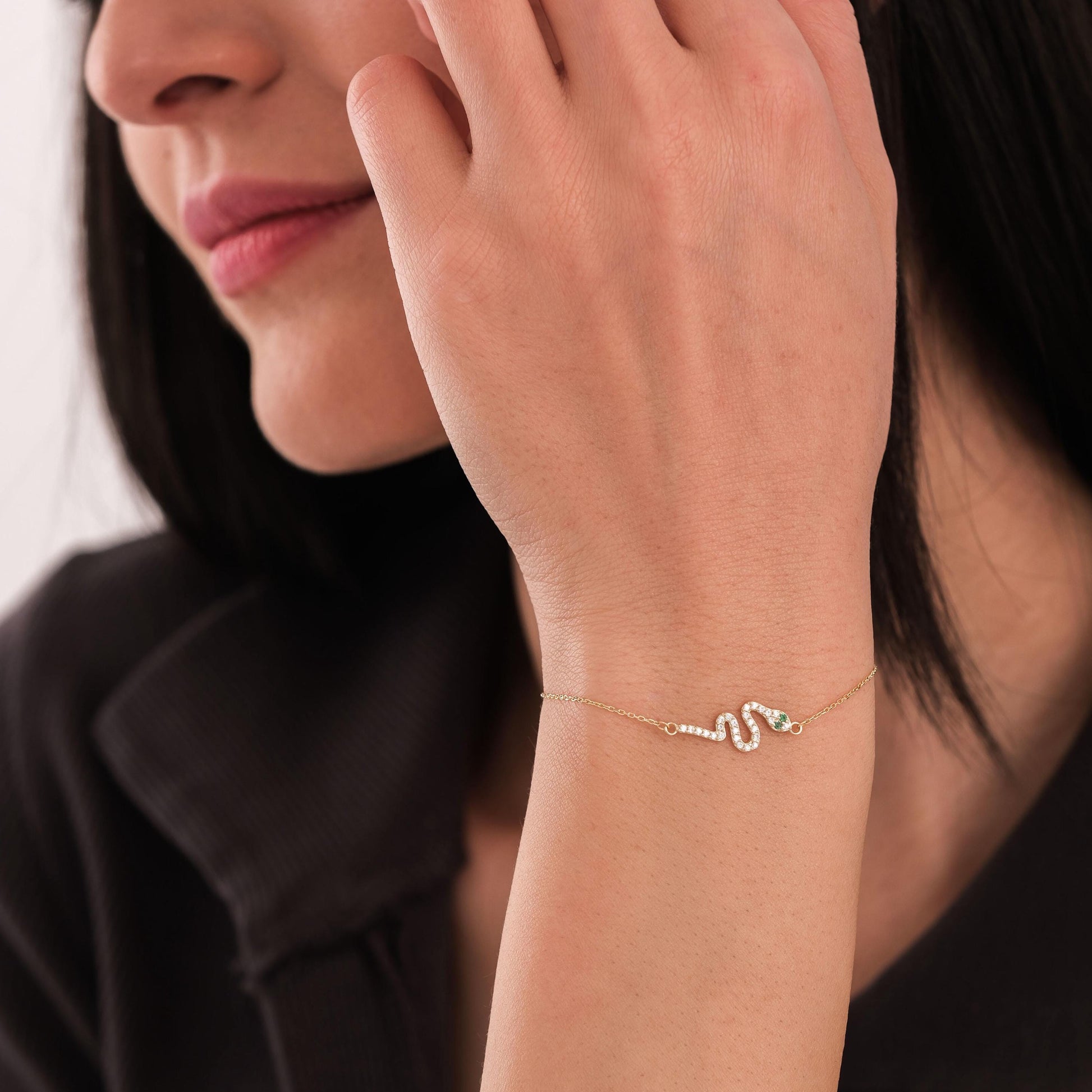 Woman wearing a 14K solid gold snake bracelet, showcasing its elegant diamond-studded design on a fine chain.