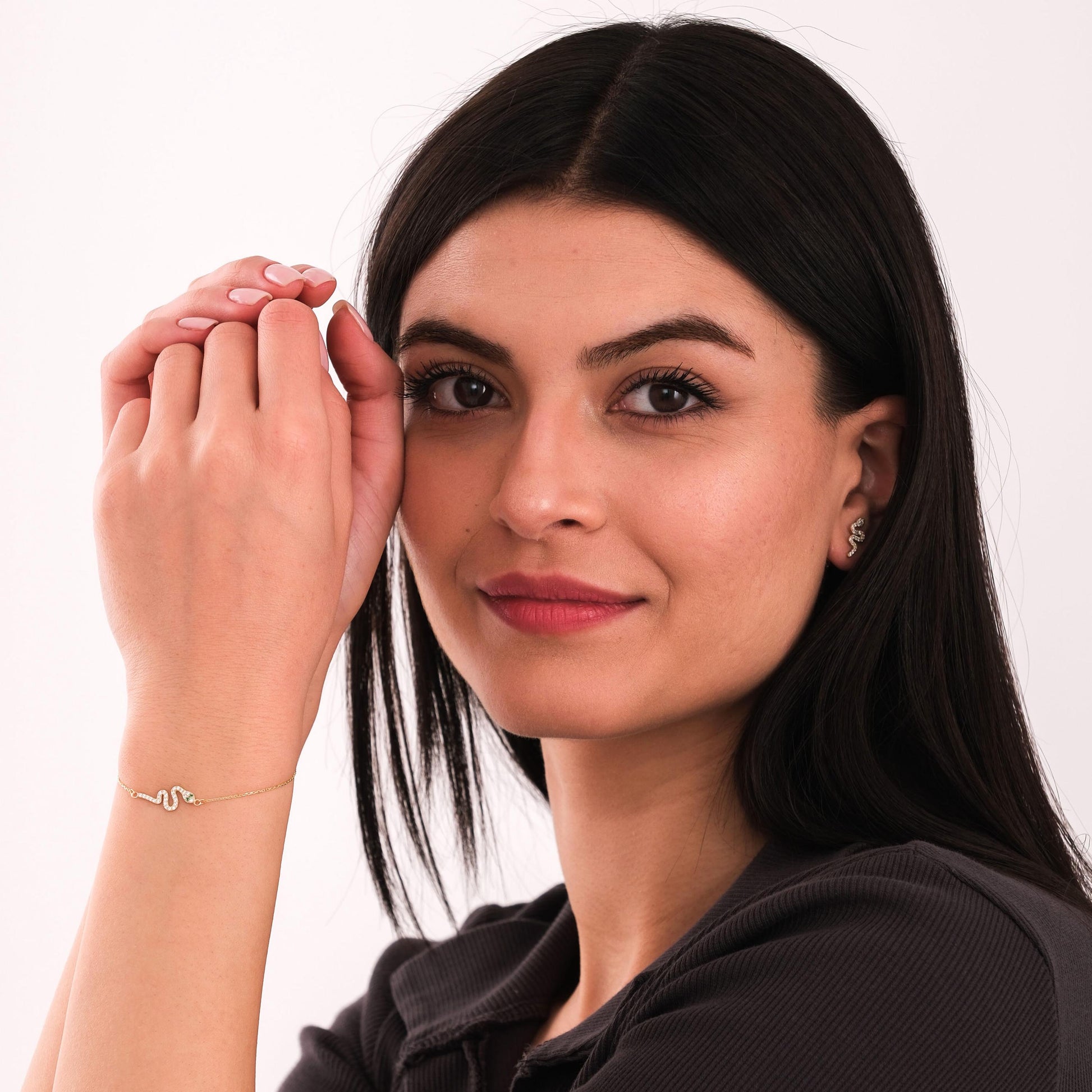 Woman posing in a dark top, wearing a matching 14K solid gold snake bracelet and snake stud earring set.