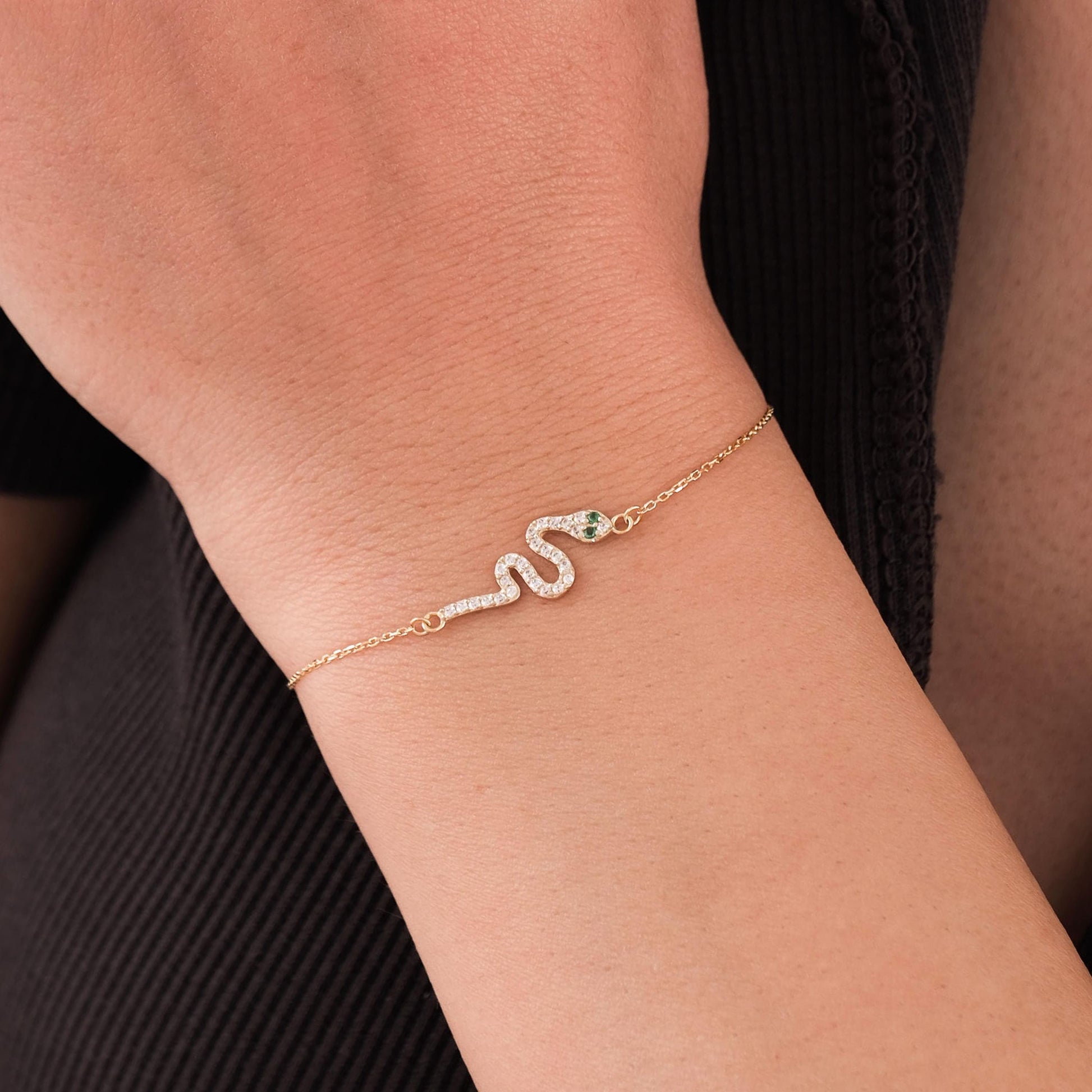 Close-up of a 14K solid gold snake bracelet with diamond accents and a green gemstone eye, worn on a wrist.