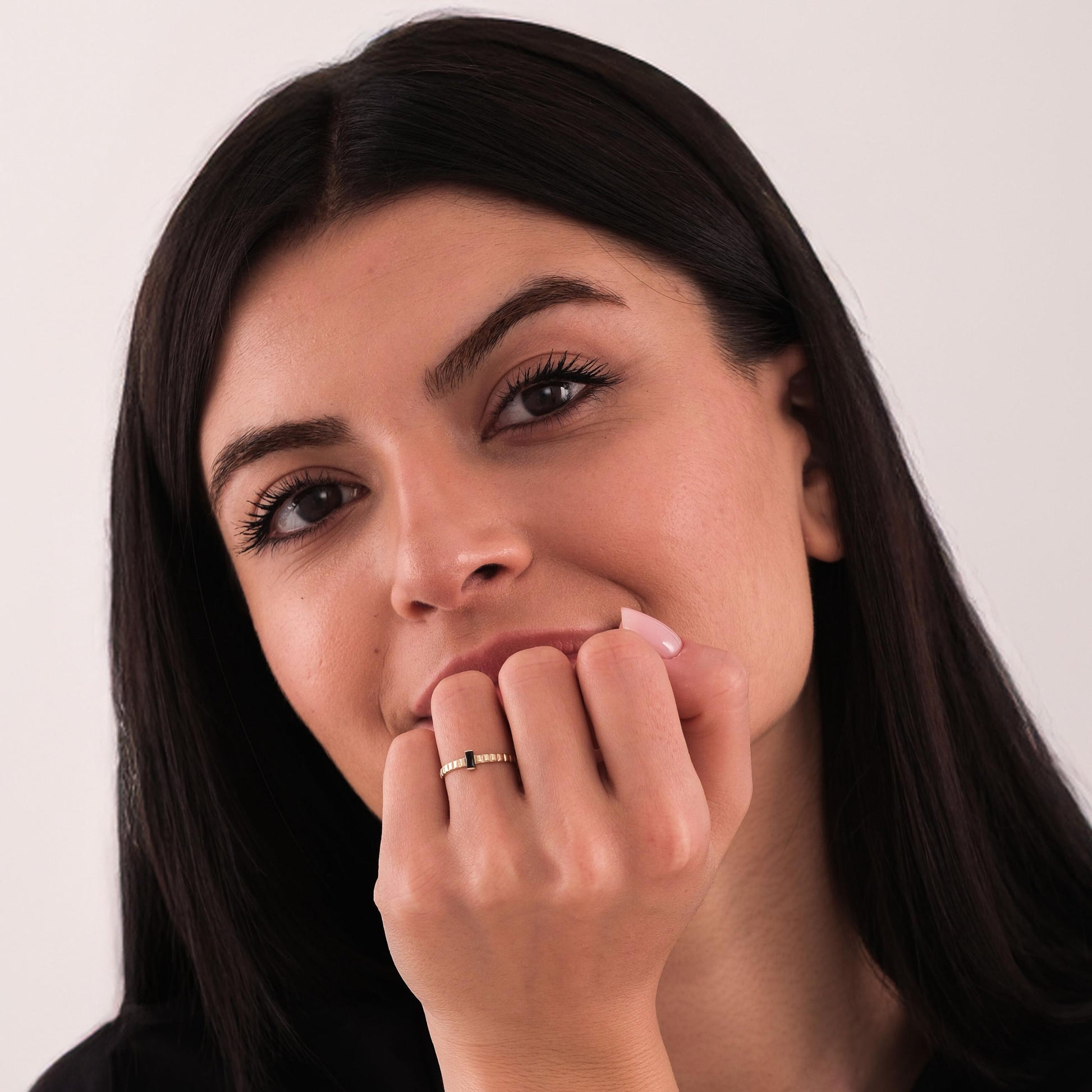 Front-facing portrait of a woman resting her chin on her hand, wearing a 14K solid gold black onyx ring.