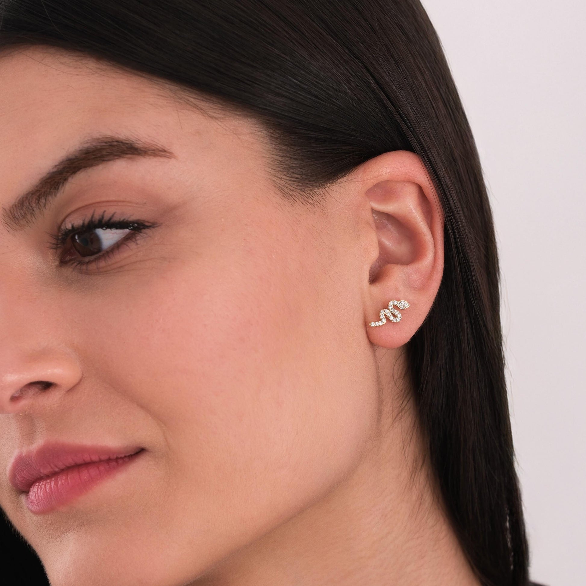 Side view of a woman wearing a 14K solid gold snake stud earring shaped in a subtle curve with sparkling stones.