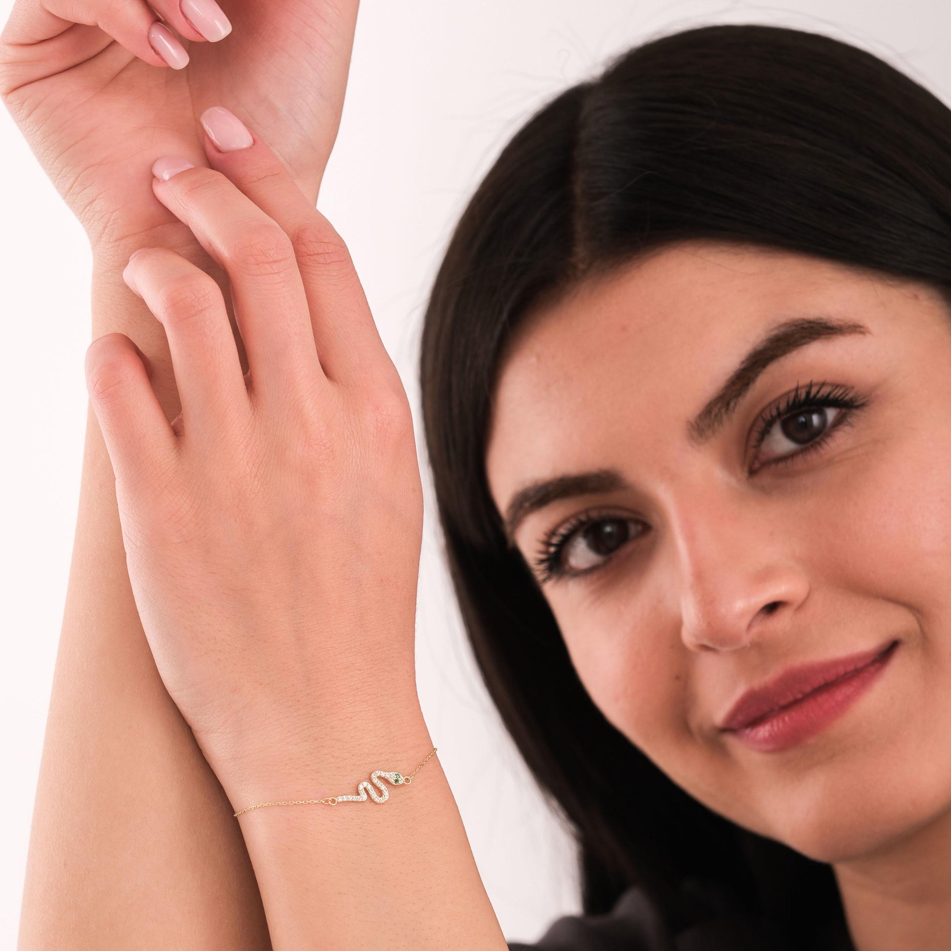 Smiling woman holding her arms up to highlight a 14K solid gold snake bracelet with sparkling stones and an emerald eye.
