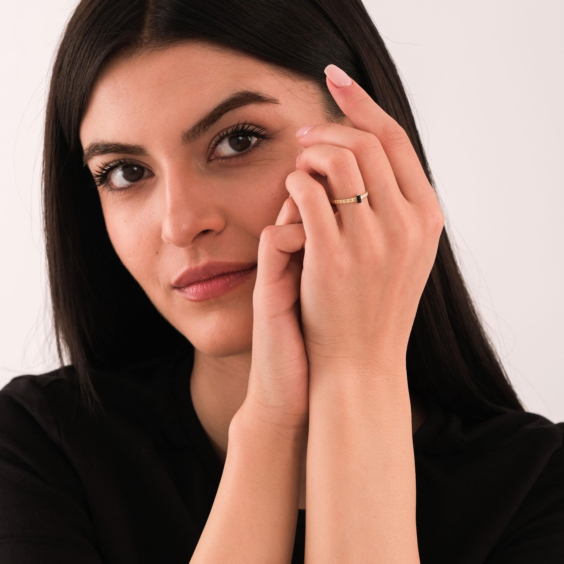 Woman holding her hands near her face, highlighting a 14K solid gold black onyx ring with a simple geometric look.